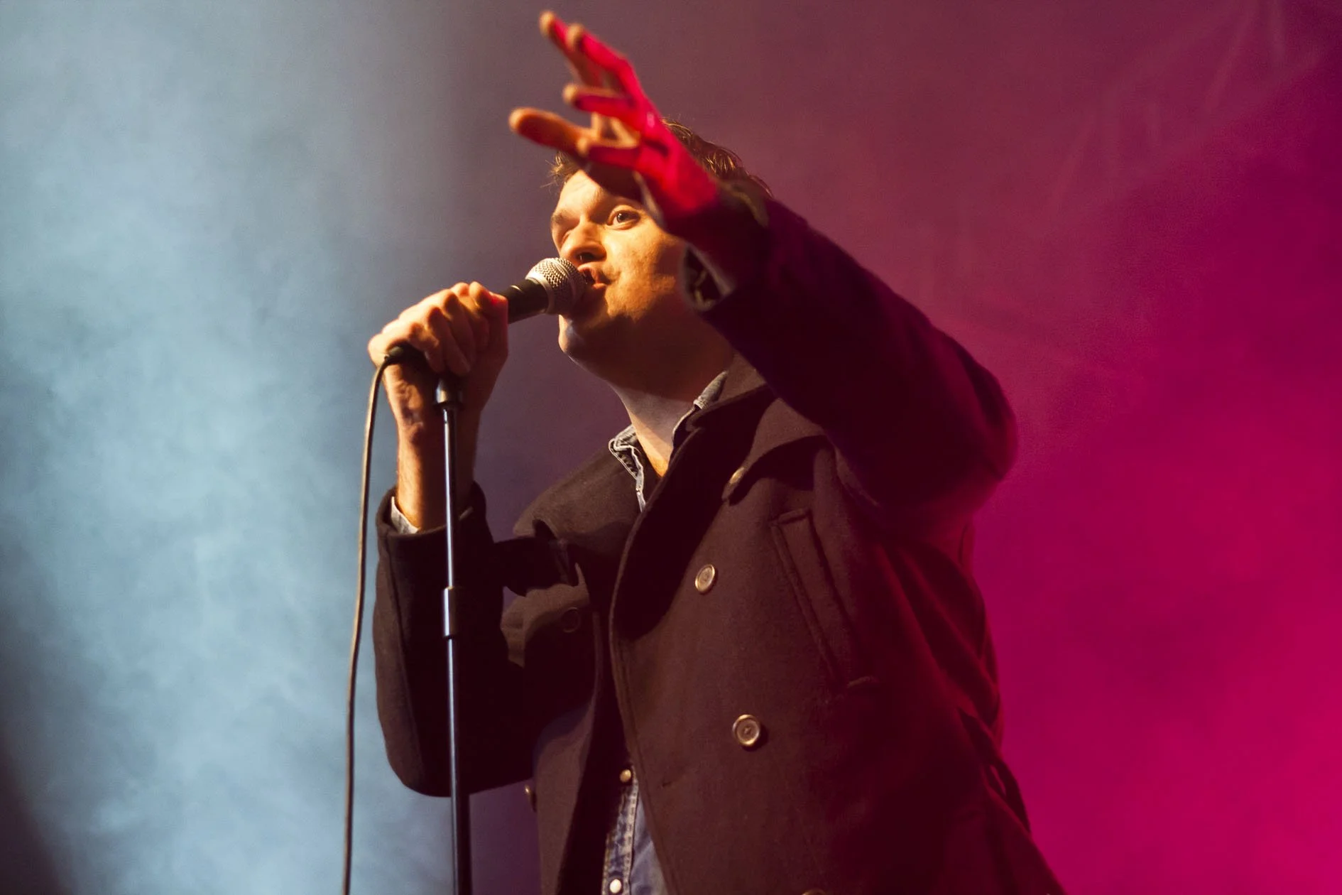 A man singing into a microphone on stage with colorful blue and pink lighting.
