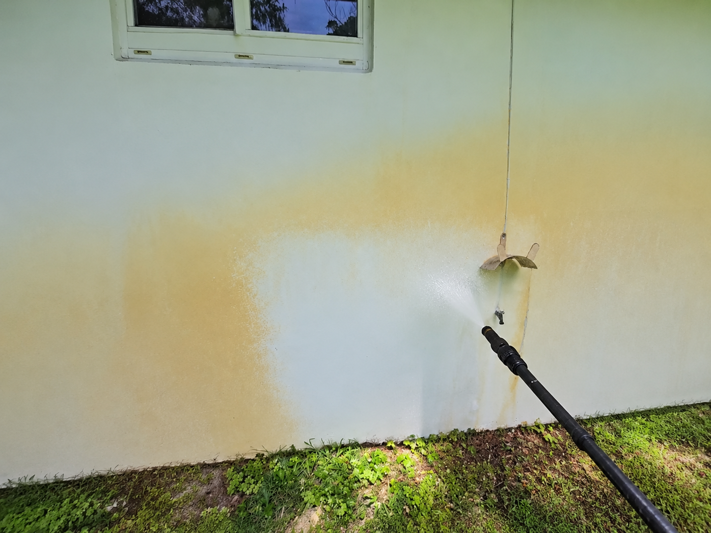 Applying house washing solution to a stained exterior wall in Miami
