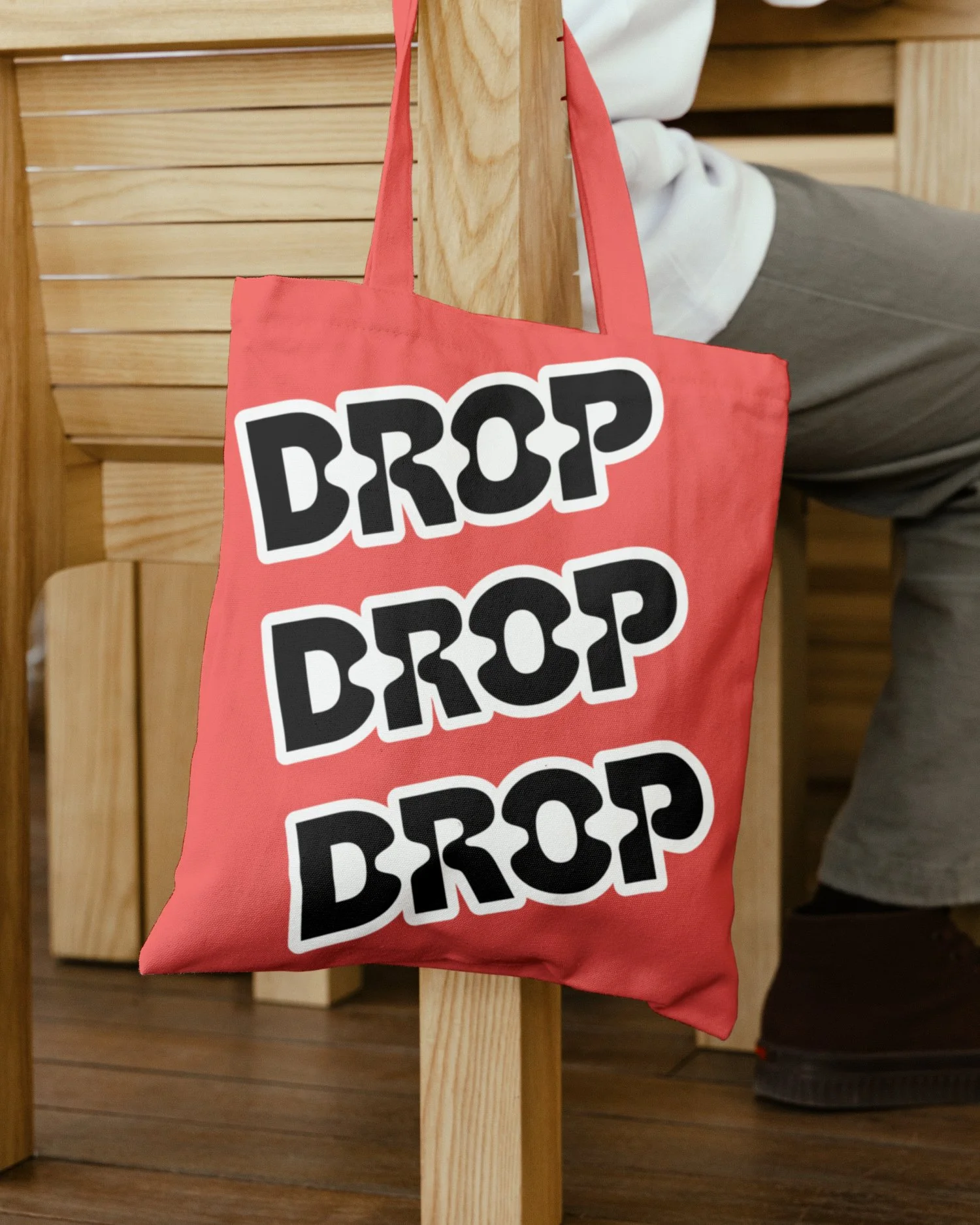 Red tote bag hanging on a wooden stand with the words "DROP DROP DROP" written repeatedly in bold black and white letters.