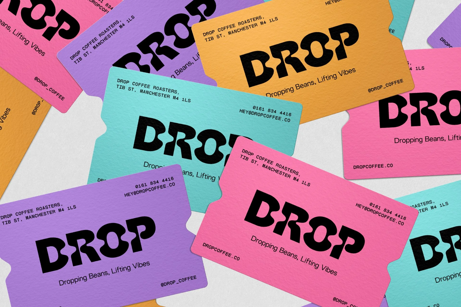 Several colorful business cards for Drop Coffee Roasters, featuring their logo and tagline 'Dropping Beans, Lifting Vibes,' with contact information and social media handle.