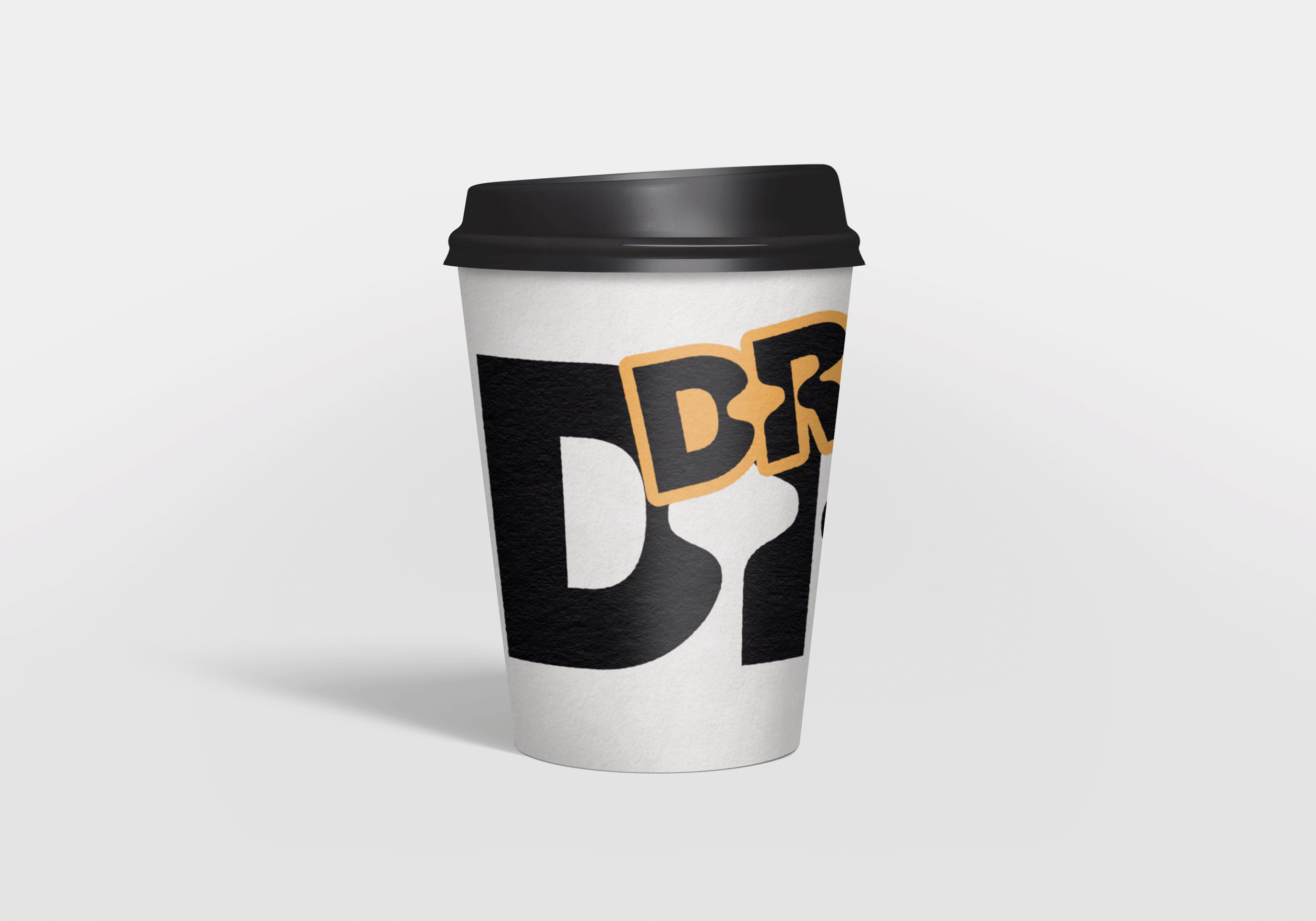 A disposable coffee cup with a black lid, featuring bold black and beige lettering on a white background.
