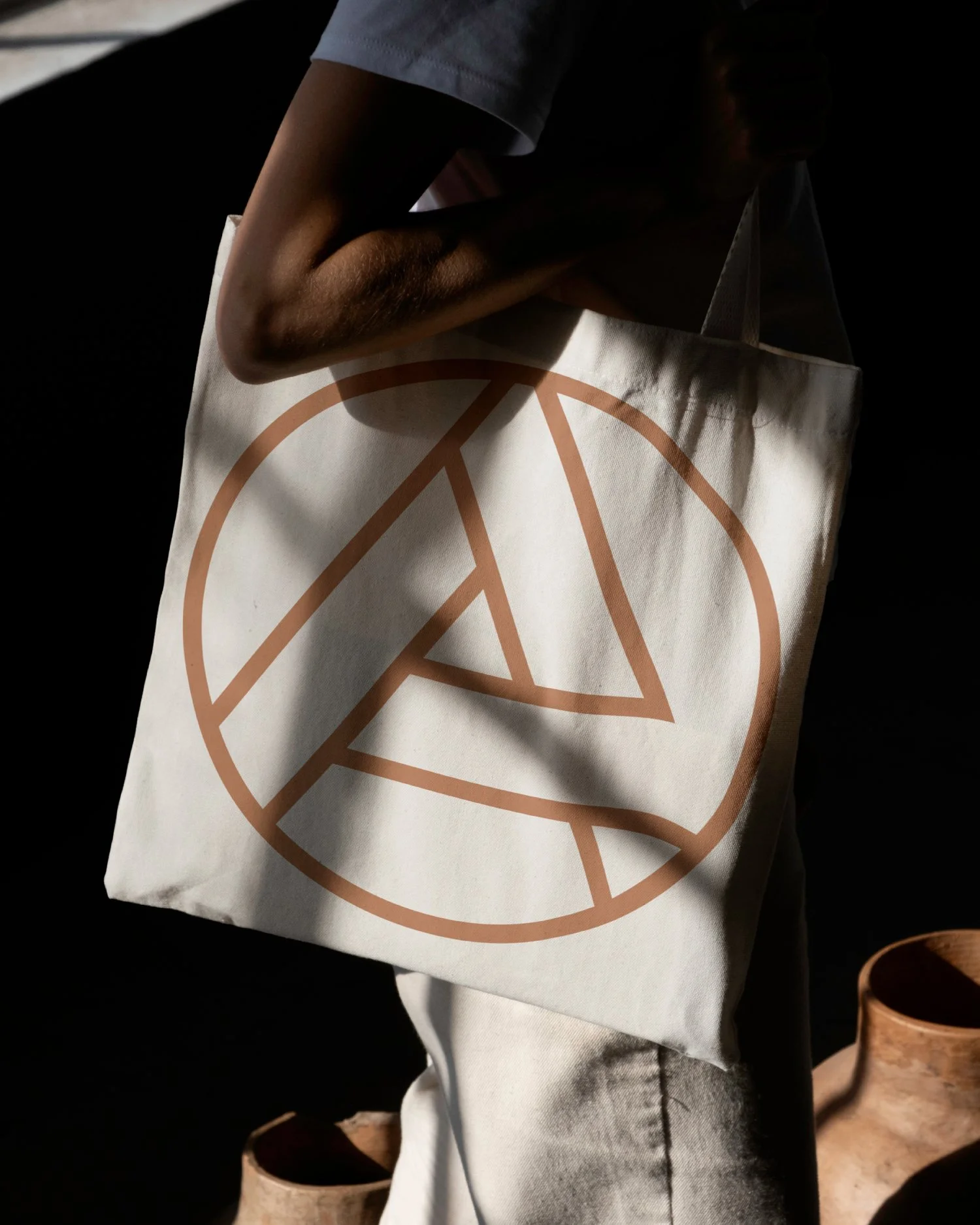 Person holding a fabric tote bag with a geometric design of a triangle within a circle in brown on a white background.