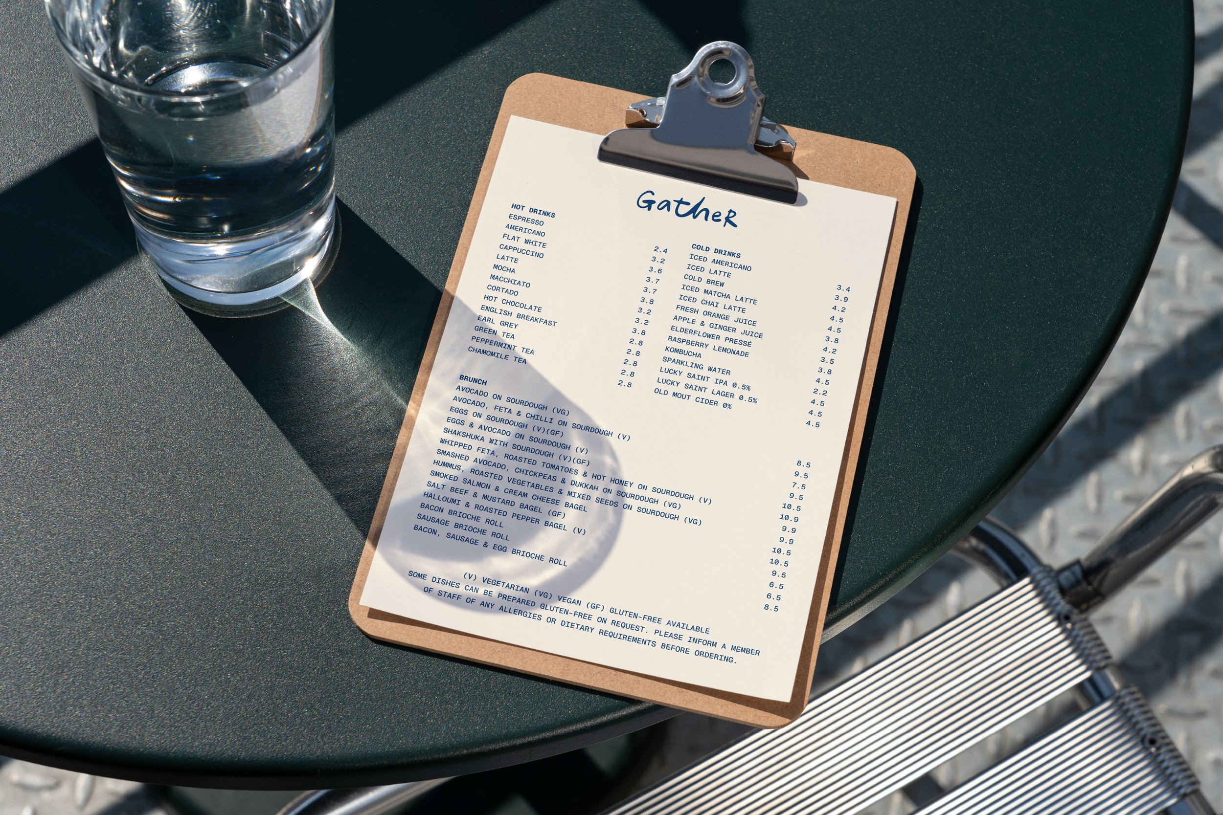A menu on a clipboard on a green table with a glass of water and a barbecue grill in the background.