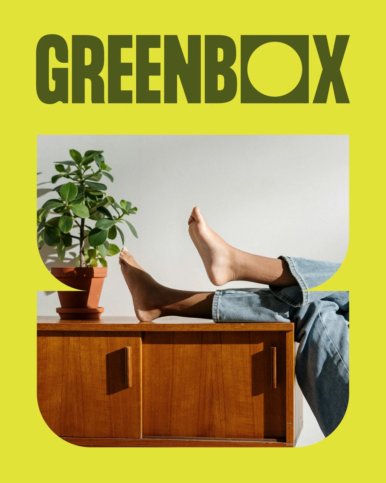 Person lying on a wooden cabinet with legs raised, near a potted plant, on a bright wall background, with a large yellow banner at the top displaying the text 'GREENBOX'.