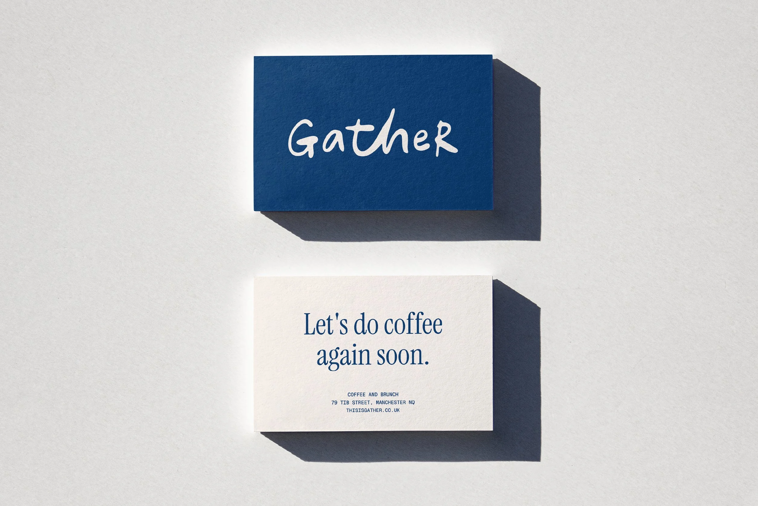 A blue card with the word 'Gather' written in white cursive text, casting a shadow on a white wall