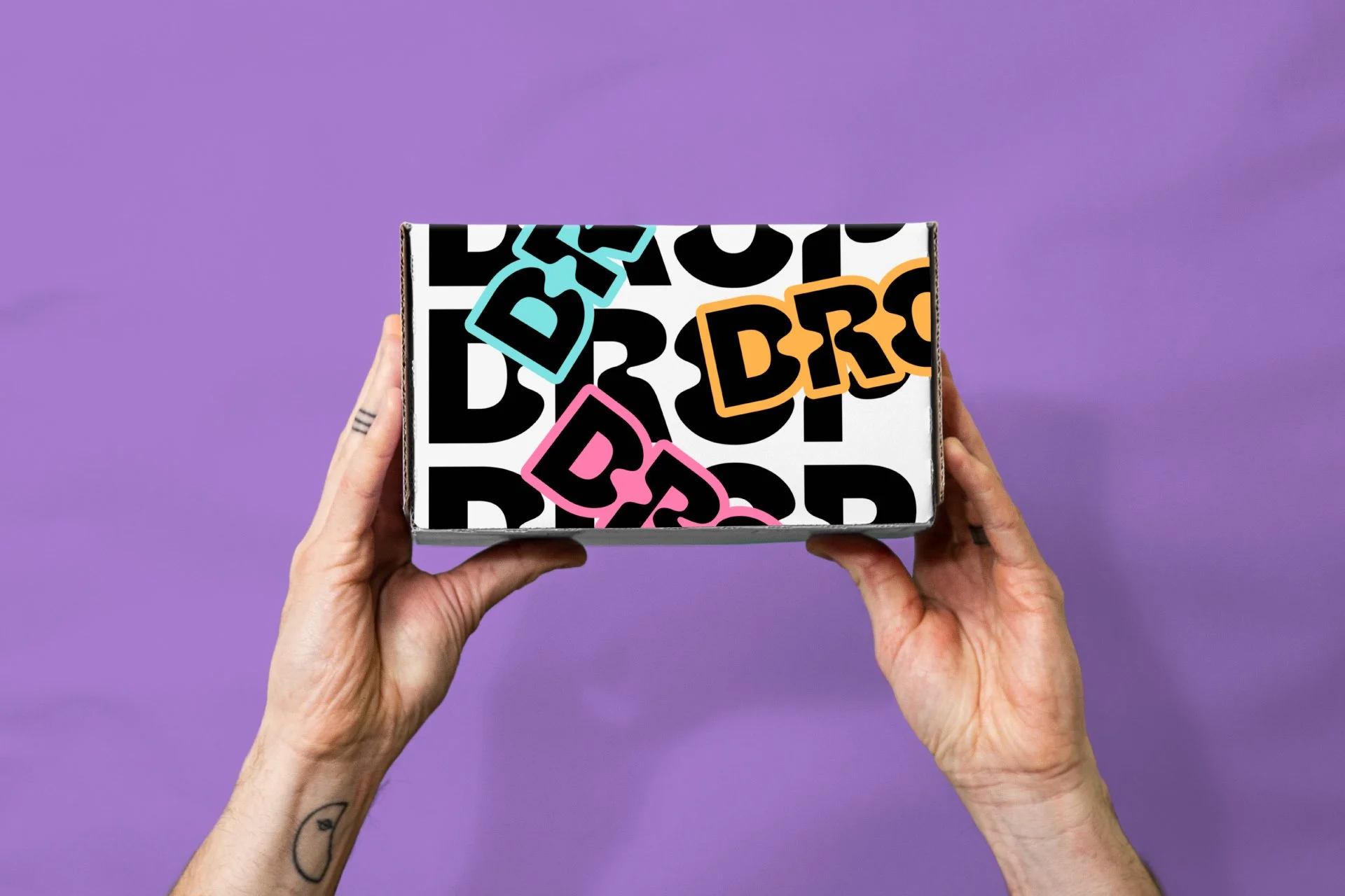 Hands holding a colorful, branded box with bold black, orange, pink, and blue text on a purple background.