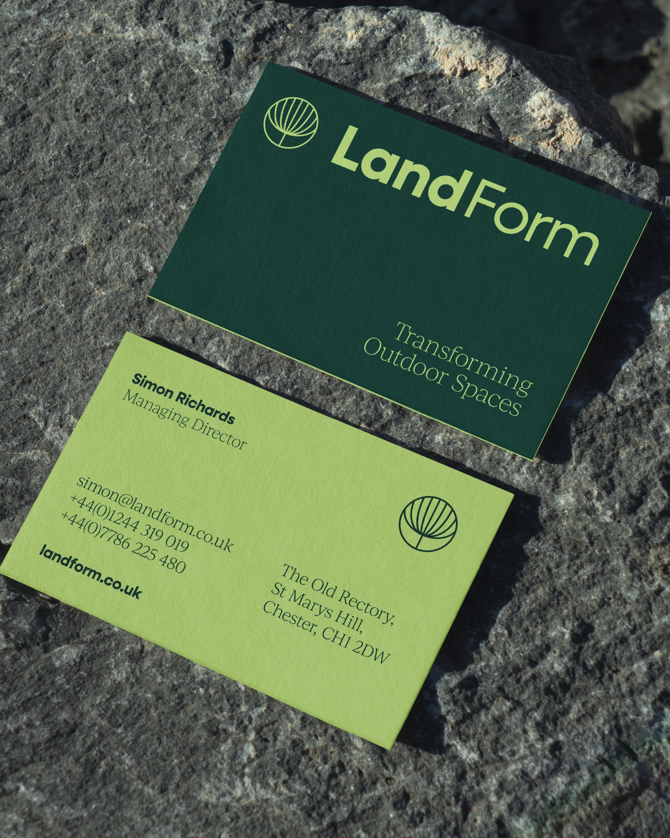 Business cards for LandForm, with the slogan 'Transforming Outdoor Spaces,' one card on stone ground and the other partly visible.