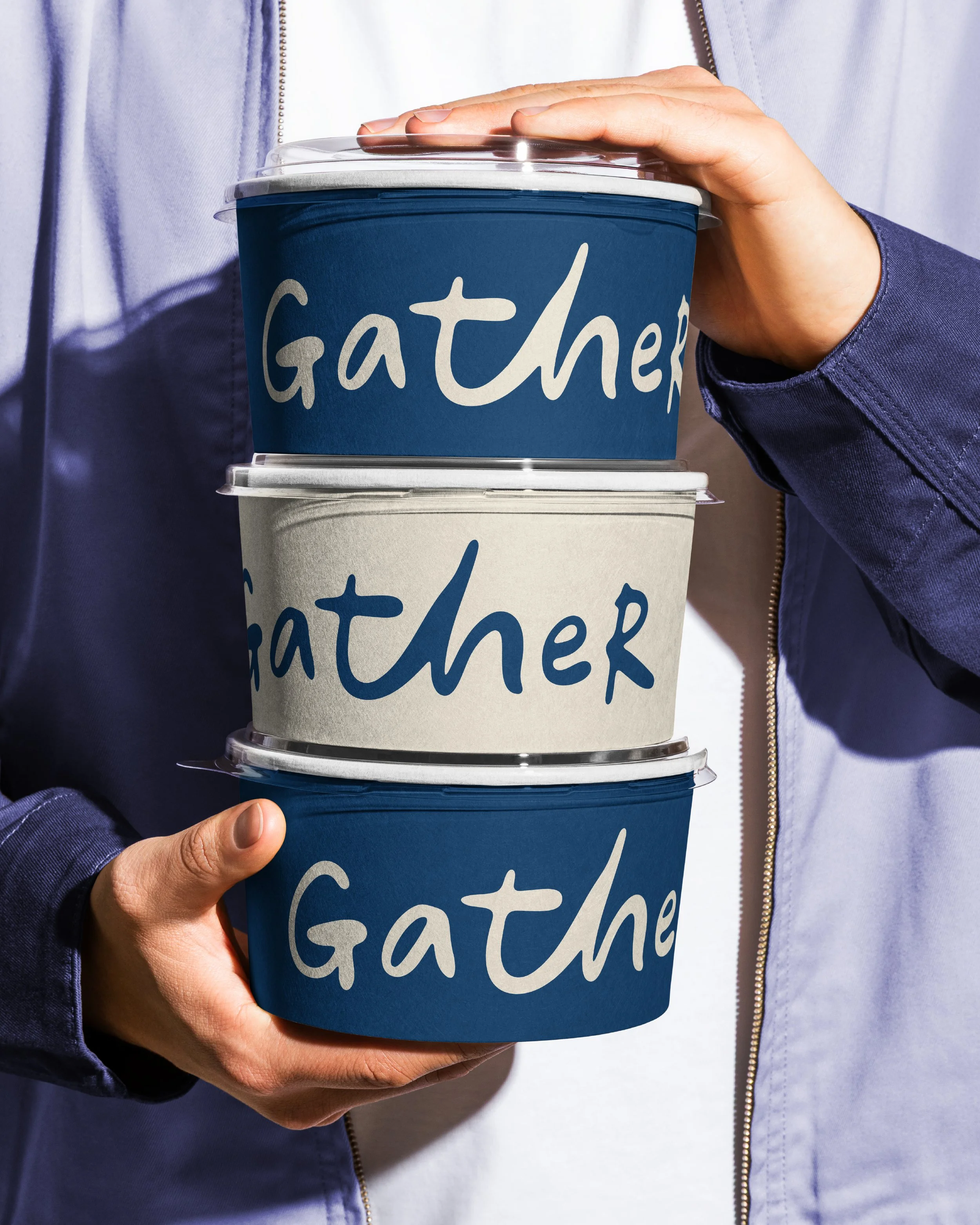 A person holding a pint of ice cream with a blue cup featuring the word 'gather' written on it in white letters.