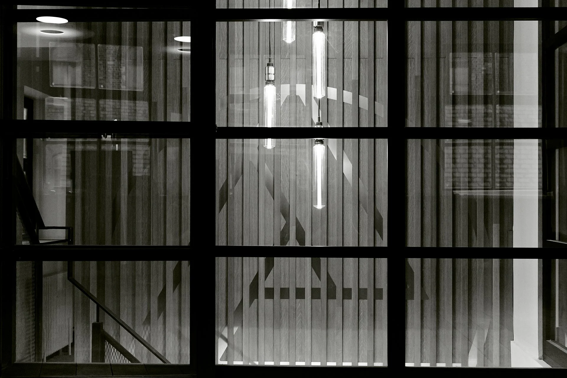 View of an interior staircase with wooden walls and hanging lights, seen through a large window divided into multiple squares.