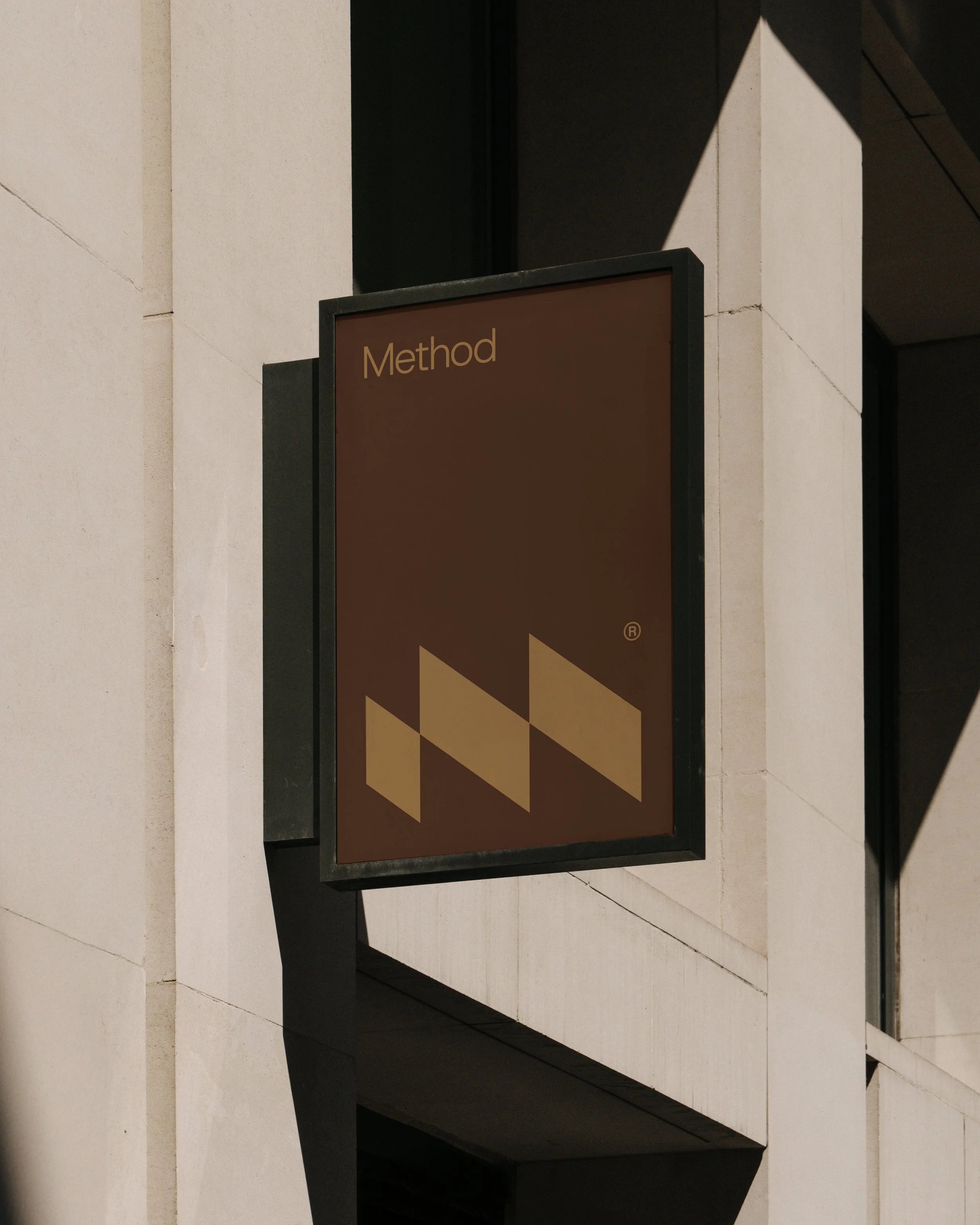 A brown and black informational sign with geometric shapes and the word "Method" in yellow on top, mounted on a black frame in front of a beige stone building.