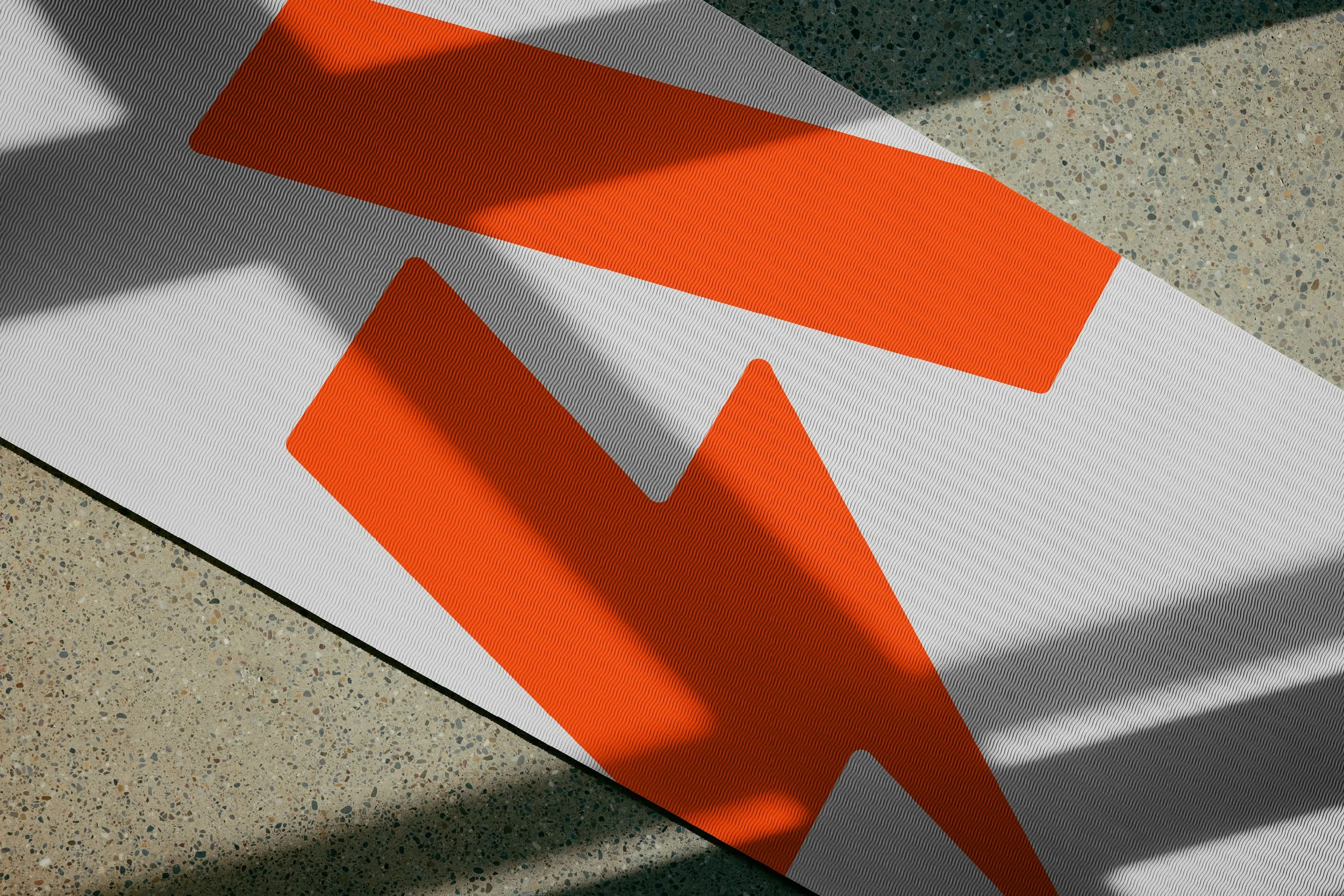 Close-up of a folded safety or construction sign with orange and gray colors on a speckled gray floor.