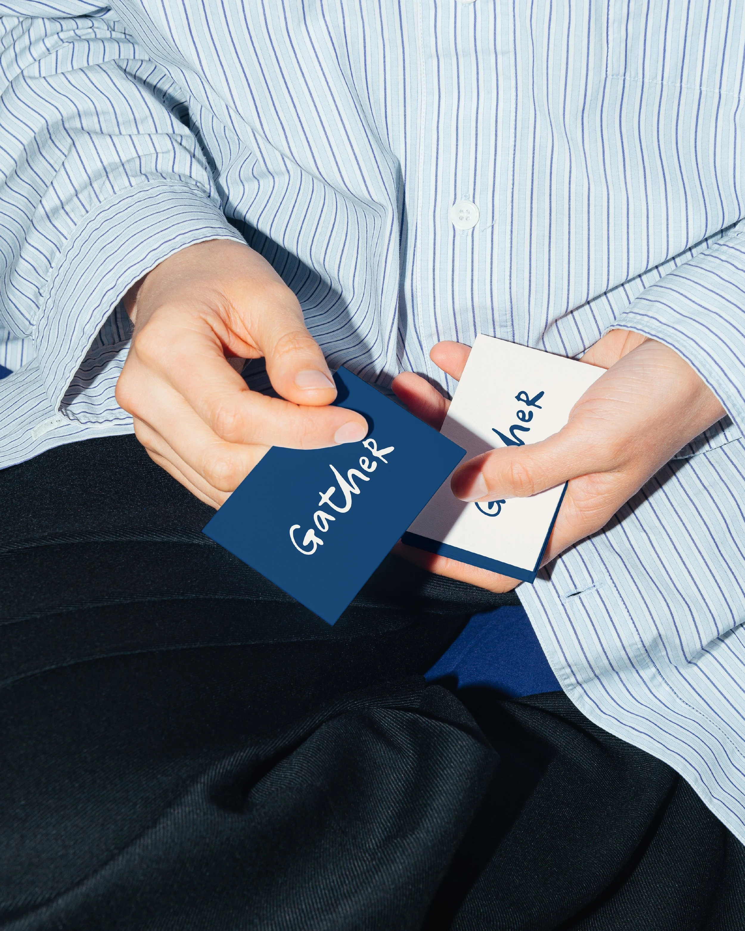 Person wearing a light blue and white striped shirt, holding a business card with blue and white colors and the word 'GATHER' on it.