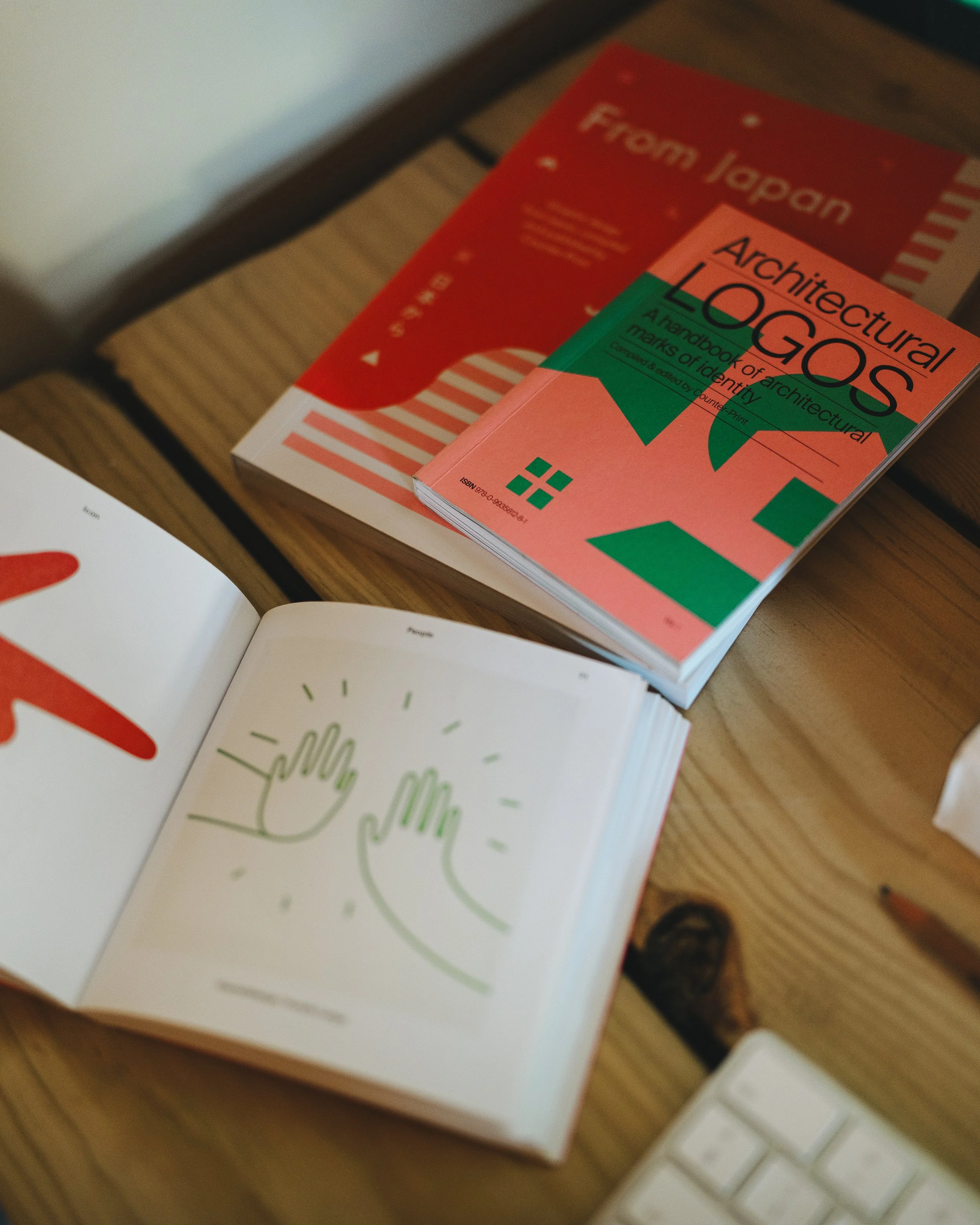 Books on a wooden desk, one book titled 'Architectural LOGOS' and an open book showing illustrations of two hands high-fiving.