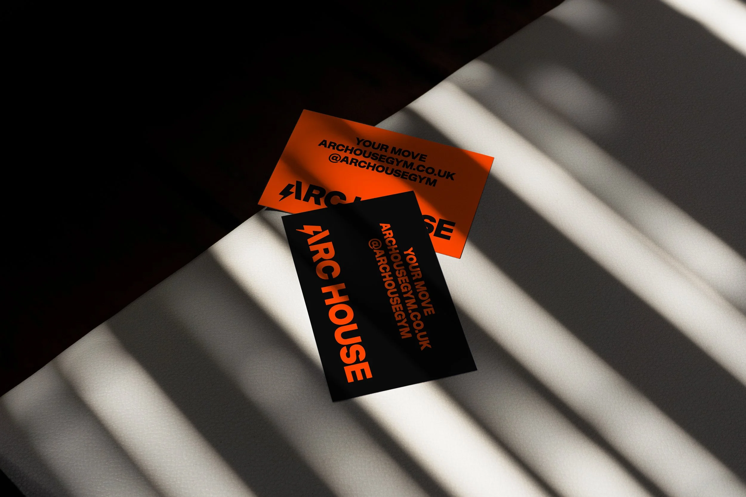 Orange and black business cards for 'Your Move' at archousegym.co.uk with @archousegym handle, placed on a white surface with shadows.