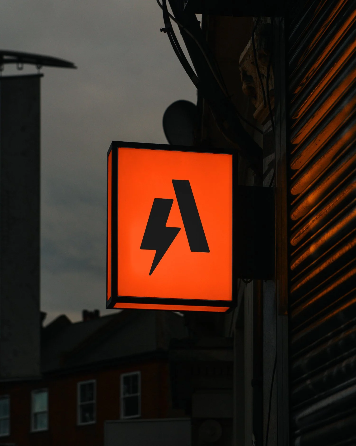 An illuminated orange sign with a black lightning bolt and the letter 'A' at night in an urban area.
