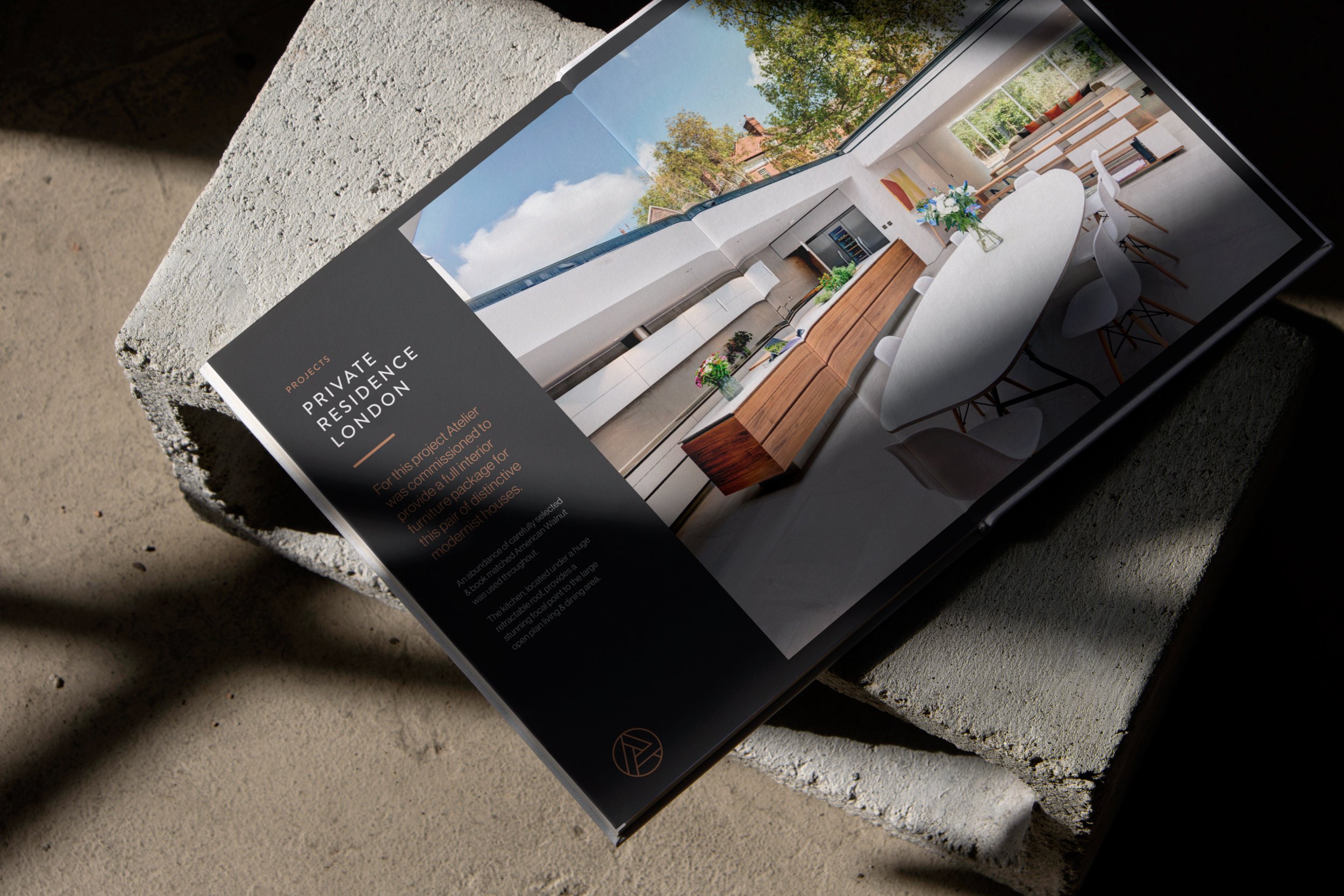 A brochure showing an interior view of a modern minimalist dining and kitchen area with large windows overlooking trees and rooftops. The brochure has a black text section on the left with project details about a private residence in London.