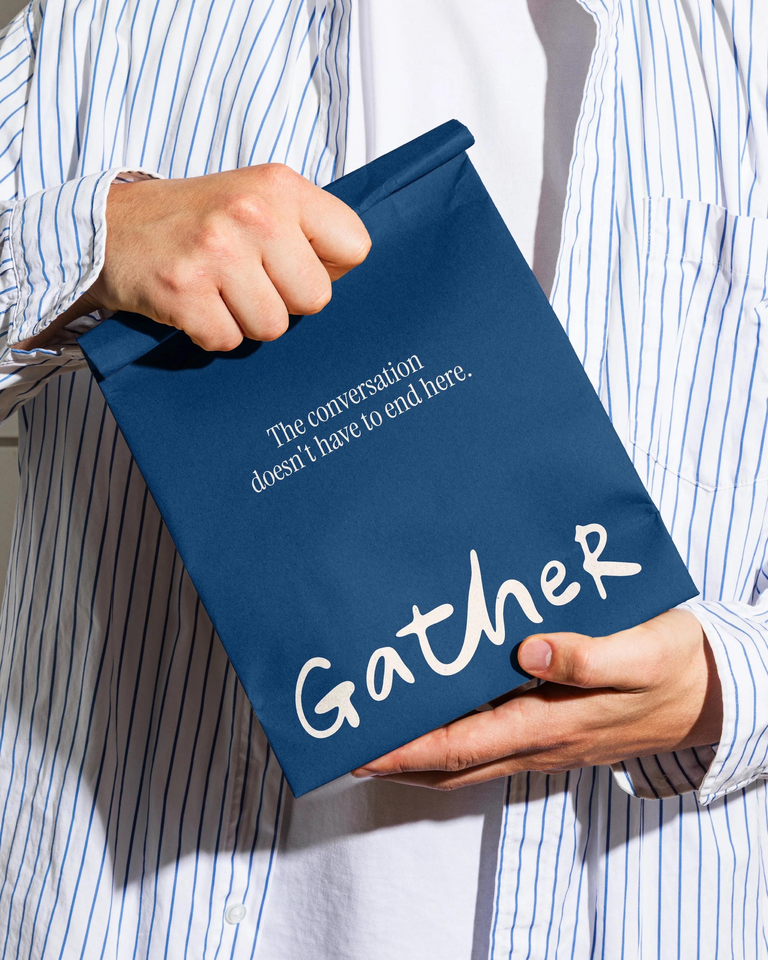 A person wearing a white and blue striped shirt holding a dark blue folder or binder with the partially visible white text that says "The conversation doesn’t have to end here".