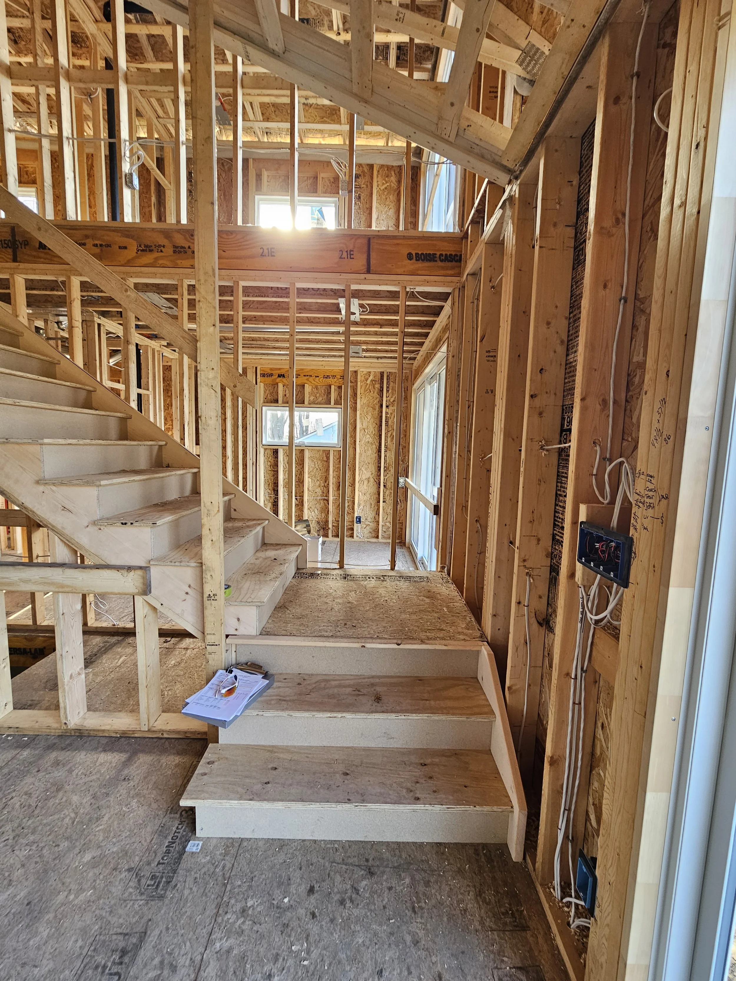Interior view of a house under construction showing wooden framing, a staircase, and wiring.