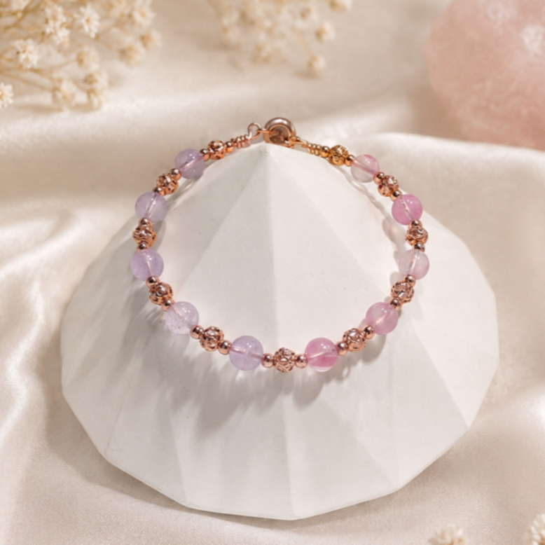 Pink and purple beaded bracelet with rose gold accents resting on a white geometric stone, with a soft pearl-colored background.