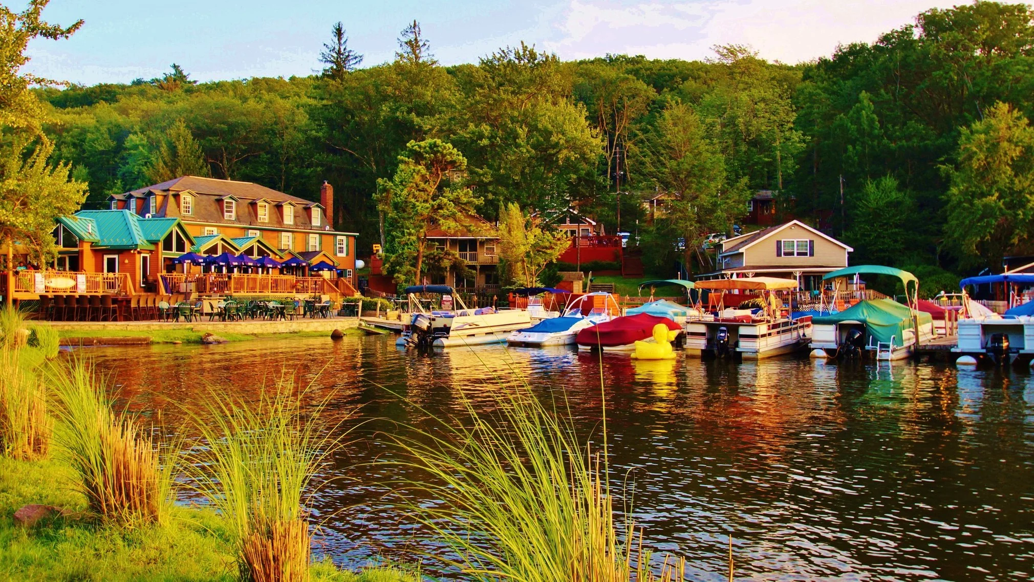 Colorful houses and boats docked along a river in a lush, green wooded area during sunset.