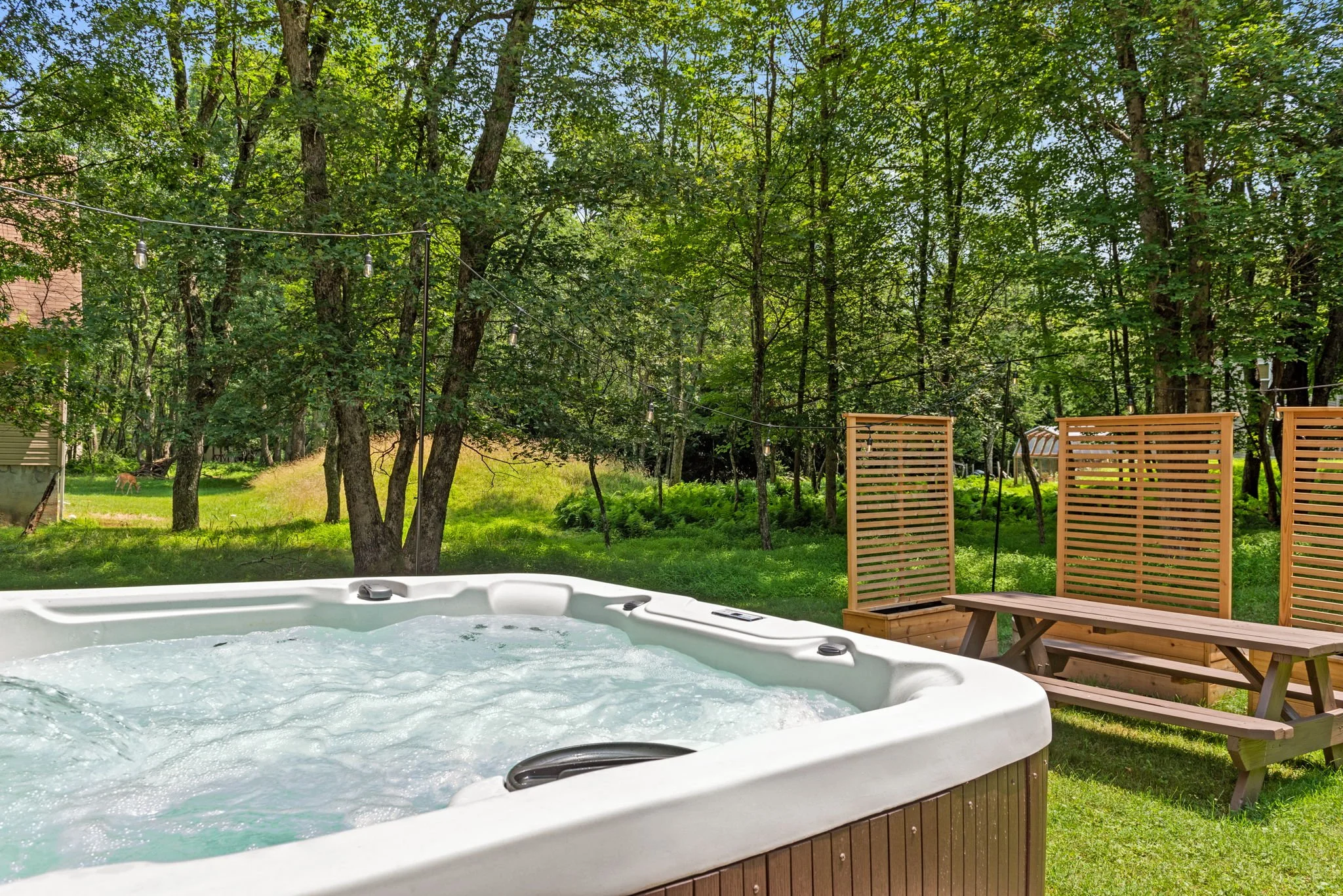 A hot tub with bubbling water on a porch overlooking a green backyard with trees and wooden fencing.