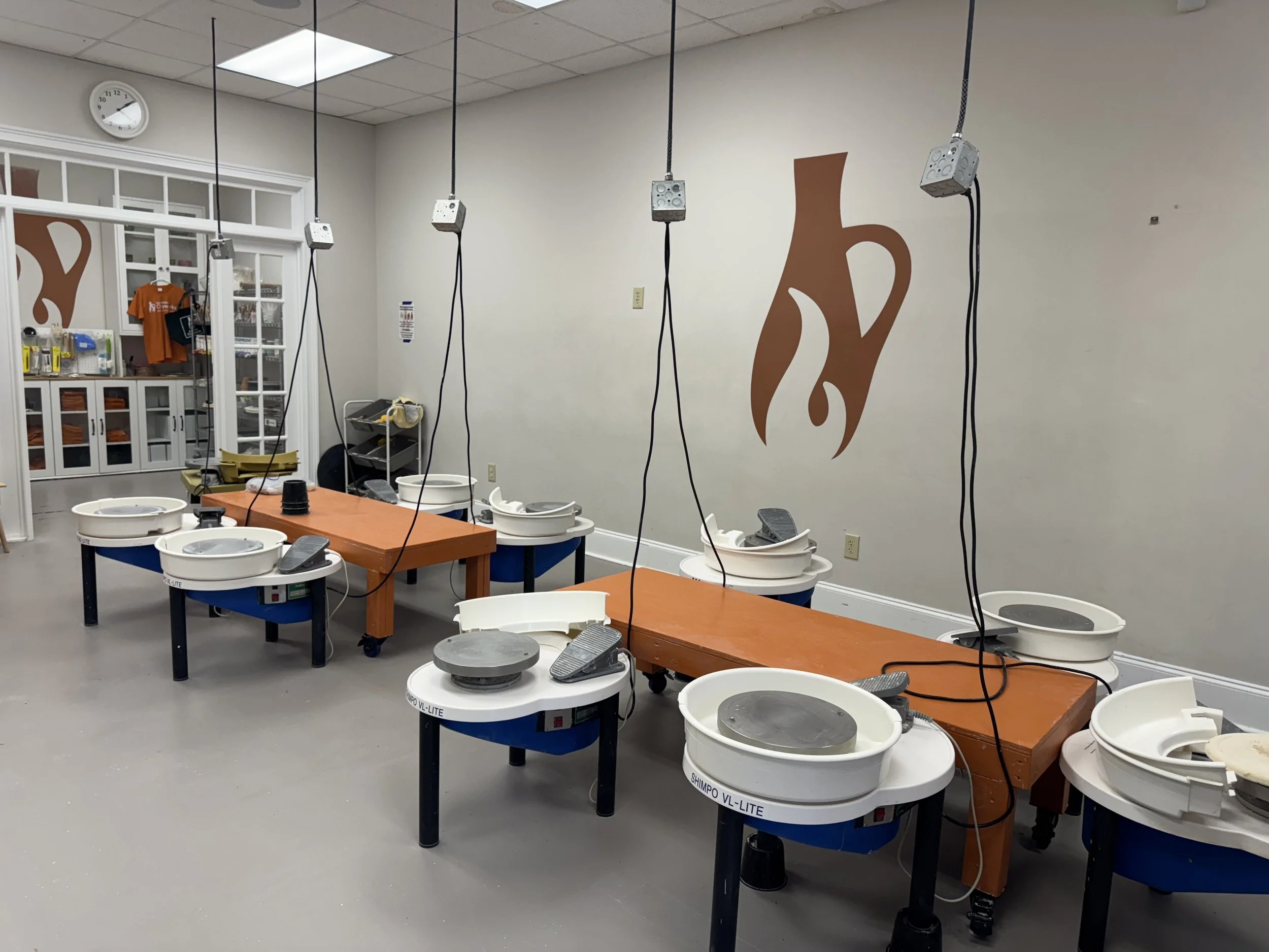 A pottery or ceramics studio with pottery wheels, work tables, and wall decorations featuring a coffee mug design.