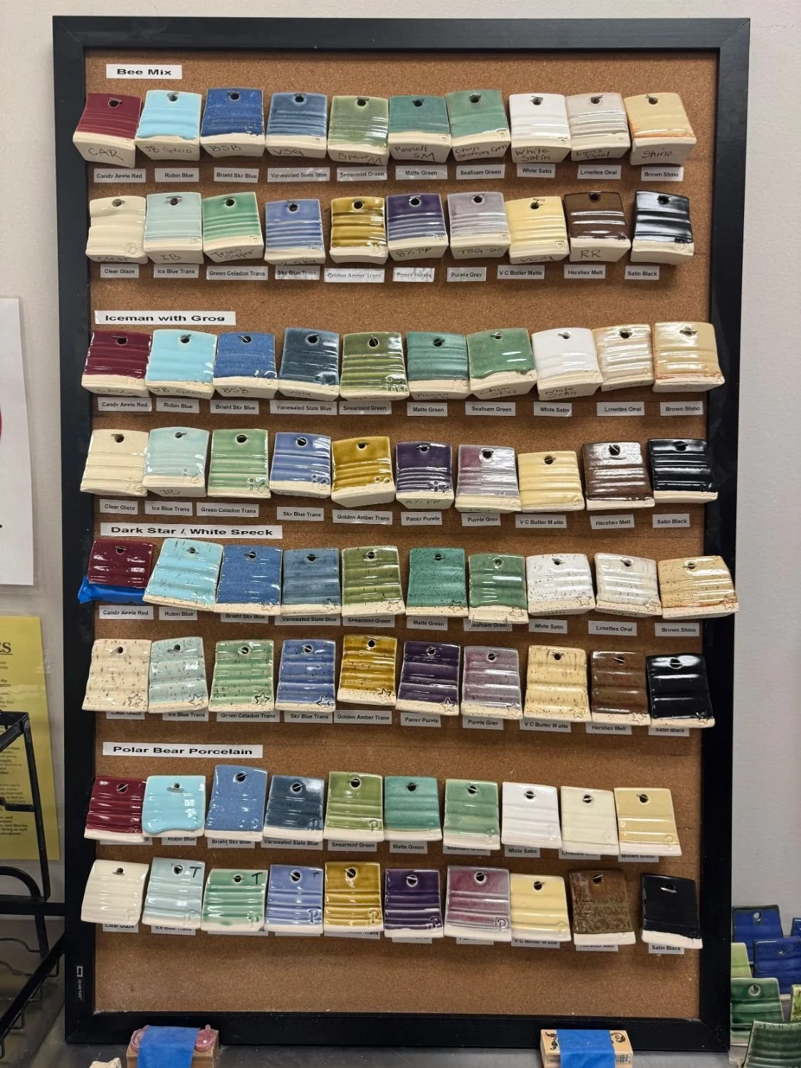 Display board of ceramic glaze samples organized in rows, labeled with different color names and finishes.