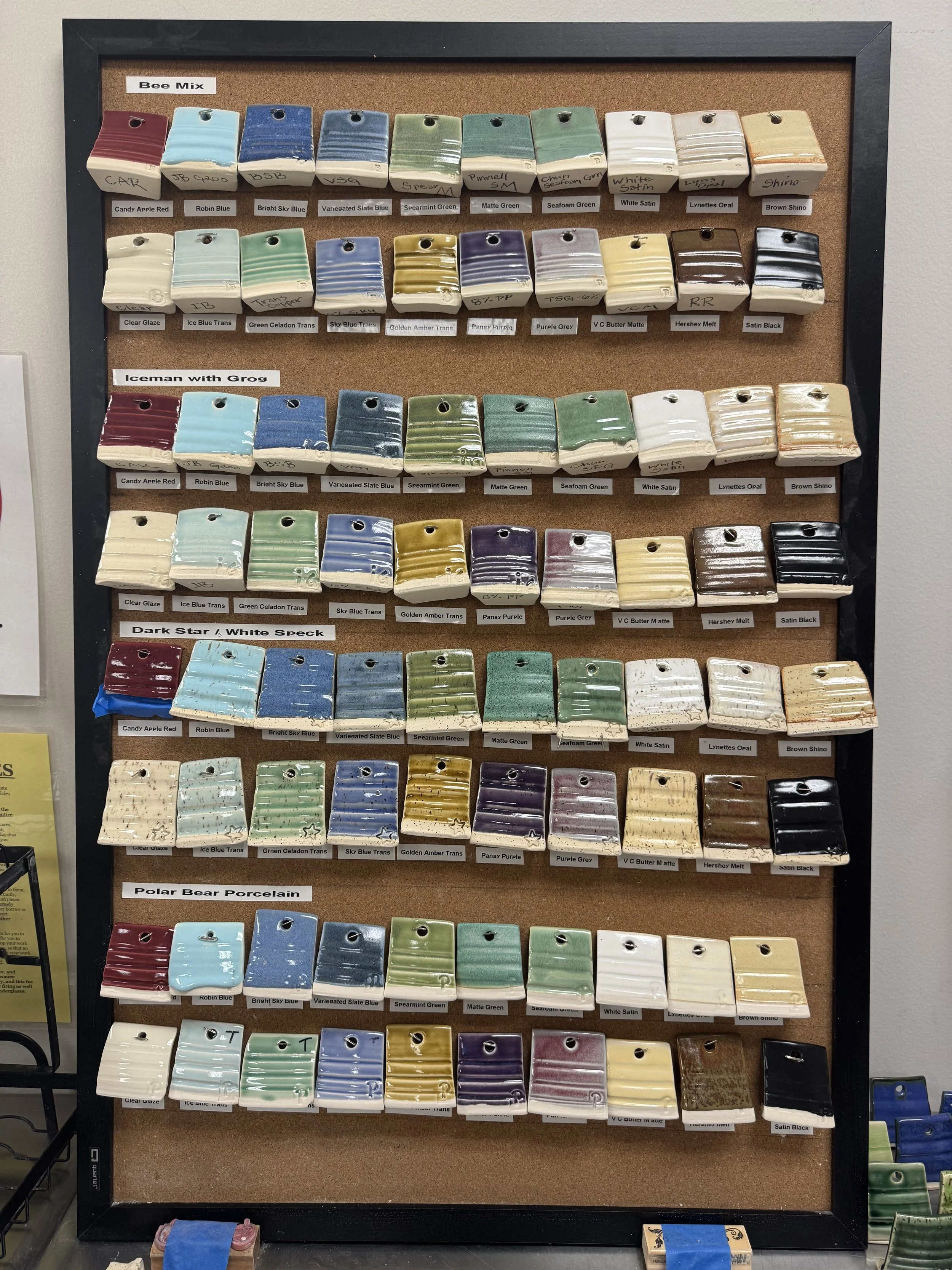 Display board with various ceramic glaze color samples organized into five categories: Bee Mix, Iceman with Grog, Dark Star & White Speck, Polar Bear Porcelain, and several unlabelled sections. Each category contains multiple small, rectangular, glazed ceramic samples.