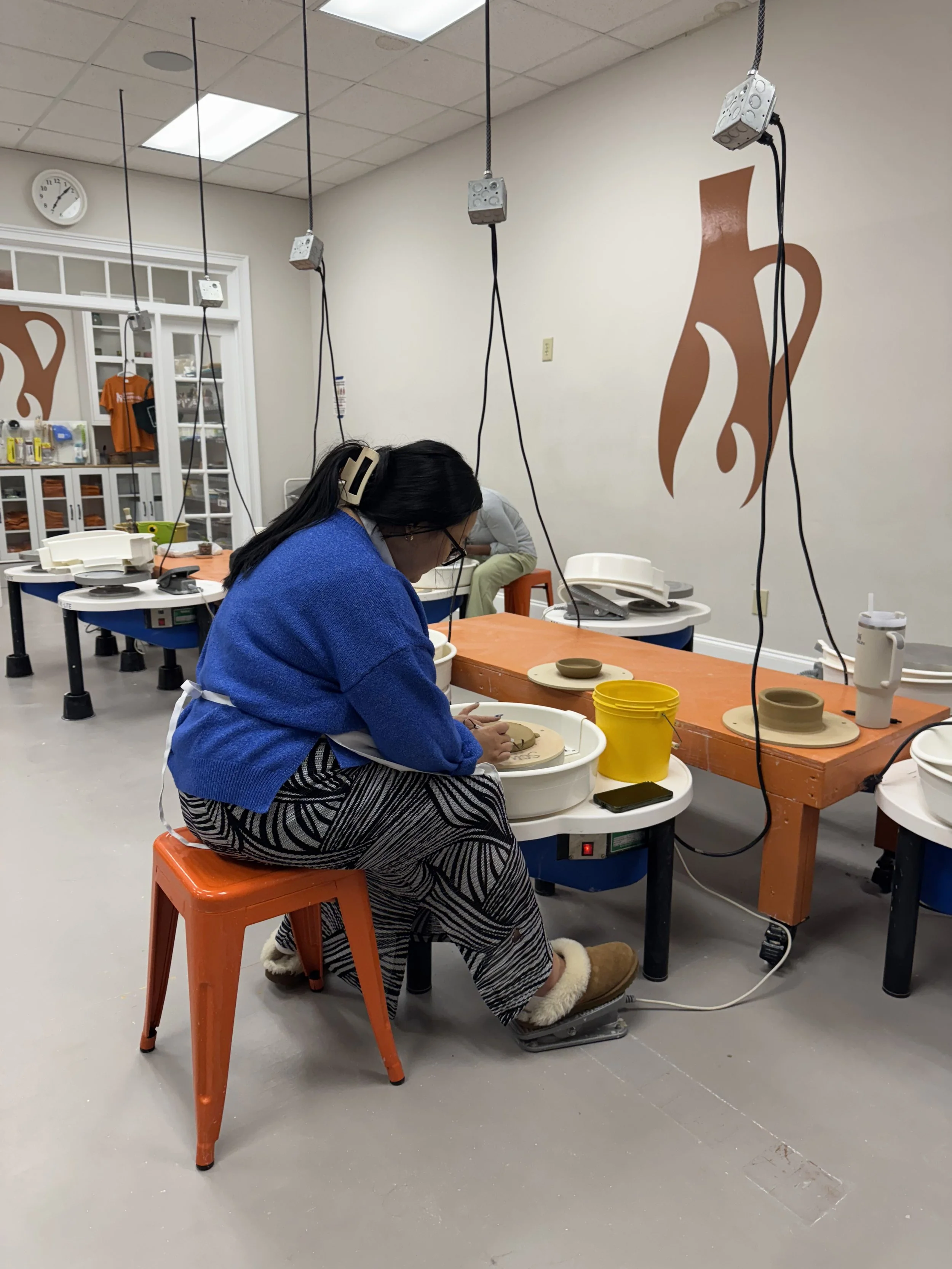 Person using a pottery wheel to make a ceramic bowl in a classroom.