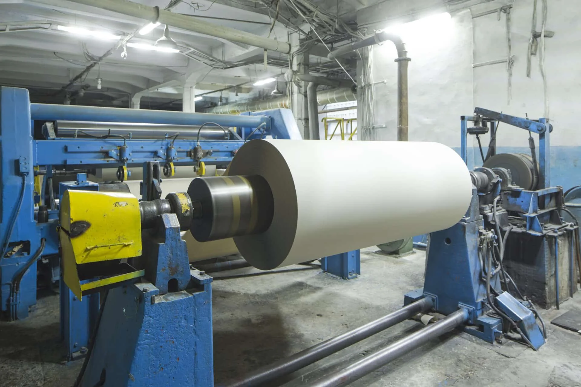 Industrial printing press machine in a factory, with a large white paper roll loaded for printing.