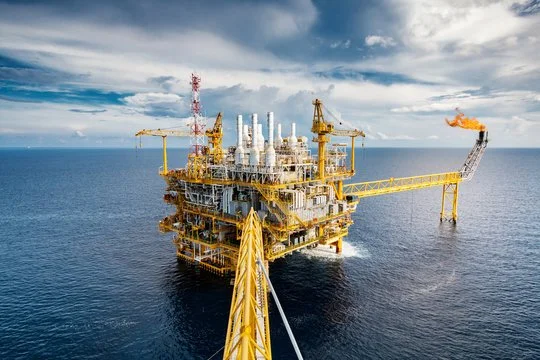 Offshore oil rig in the ocean with cranes and equipment, under a partly cloudy sky.