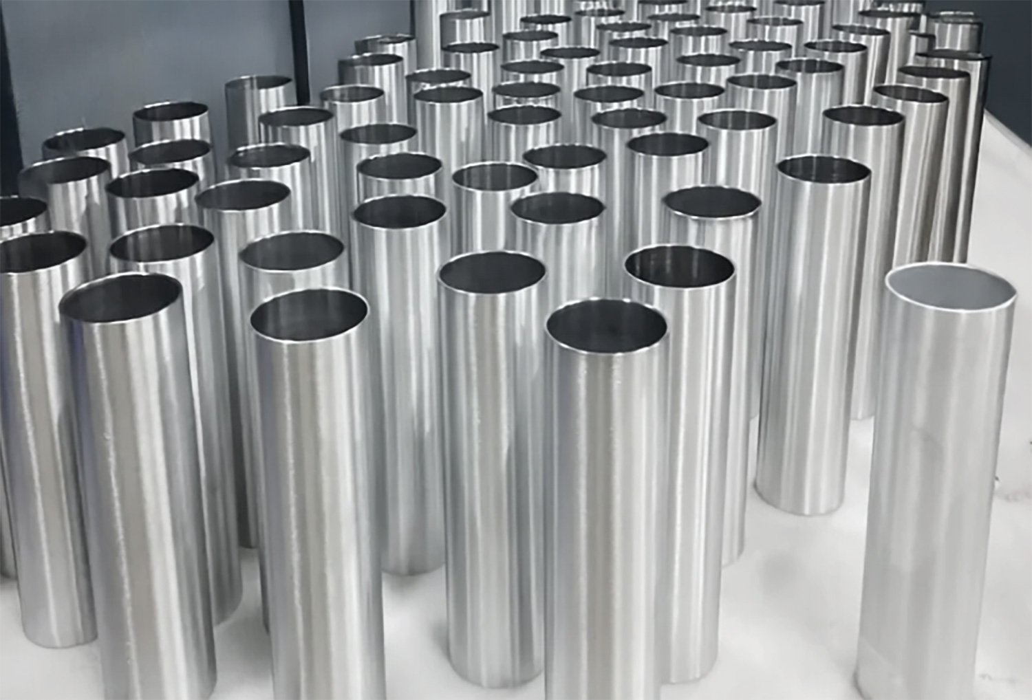 Multiple vertical cylindrical metal tubes arranged in rows on a white surface.