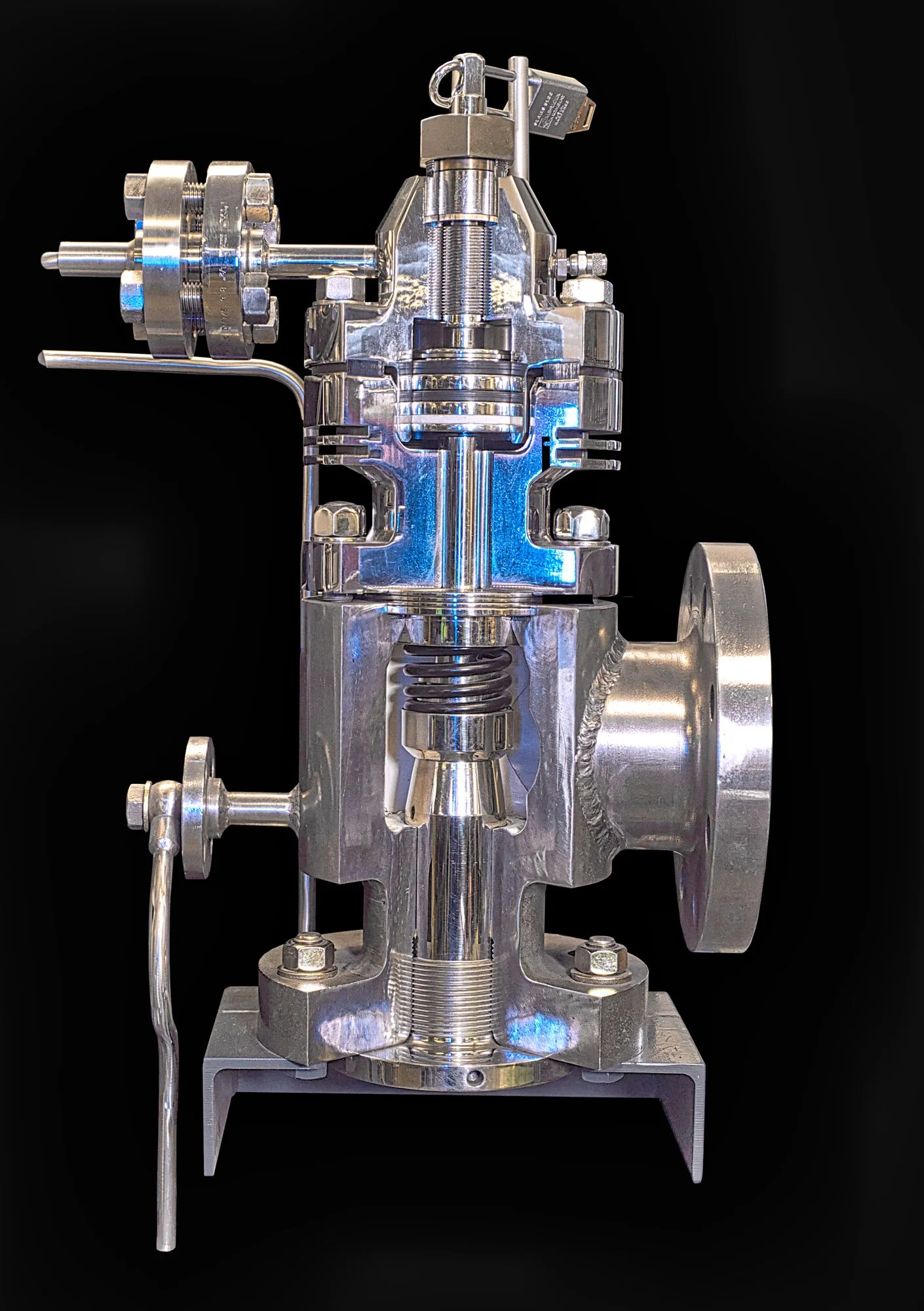 Close-up of a shiny, metallic, industrial valve or pump component with various bolts, fittings, and a large circular opening, set against a black background.