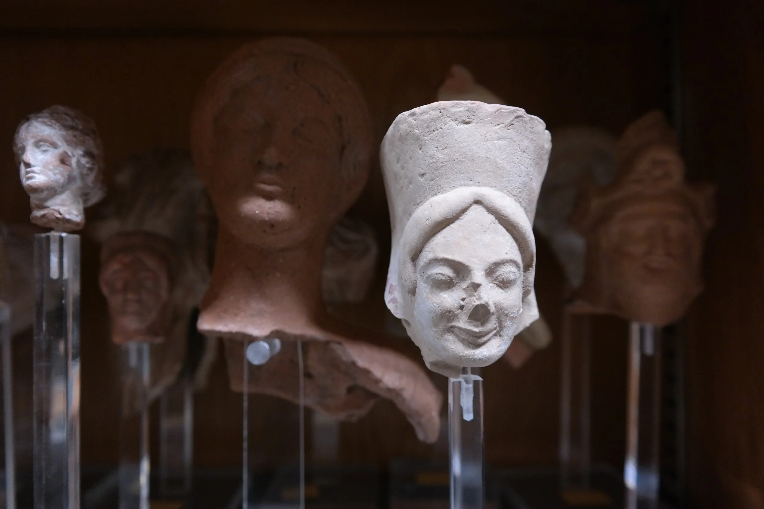 Fragmente griechischer Terrakottafigurinen aus der Antikensammlung der Universität Heidelberg. Im Vordergrund: ein gut erhaltener Kopf aus Tarent (Unteritalien), datiert auf das 6. Jahrhundert v. Chr. – Beispiel archaischer Keramikkunst.