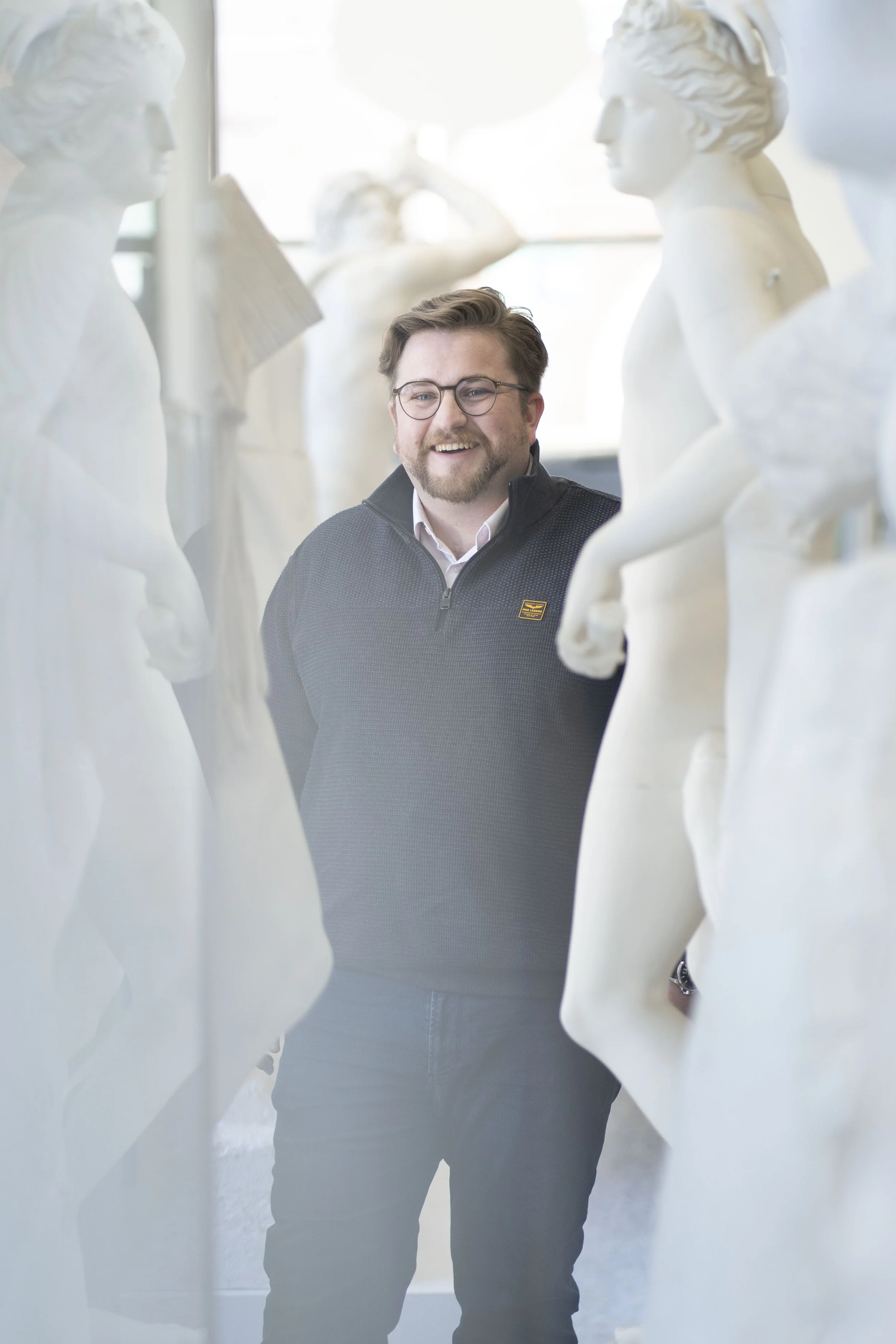 Porträt von Sascha Marschner, Vorstand der Novus Stiftung, freundlich und lachend zwischen Gipsabgüssen antiker Statuen in der Antikensammlung der Universität Heidelberg.