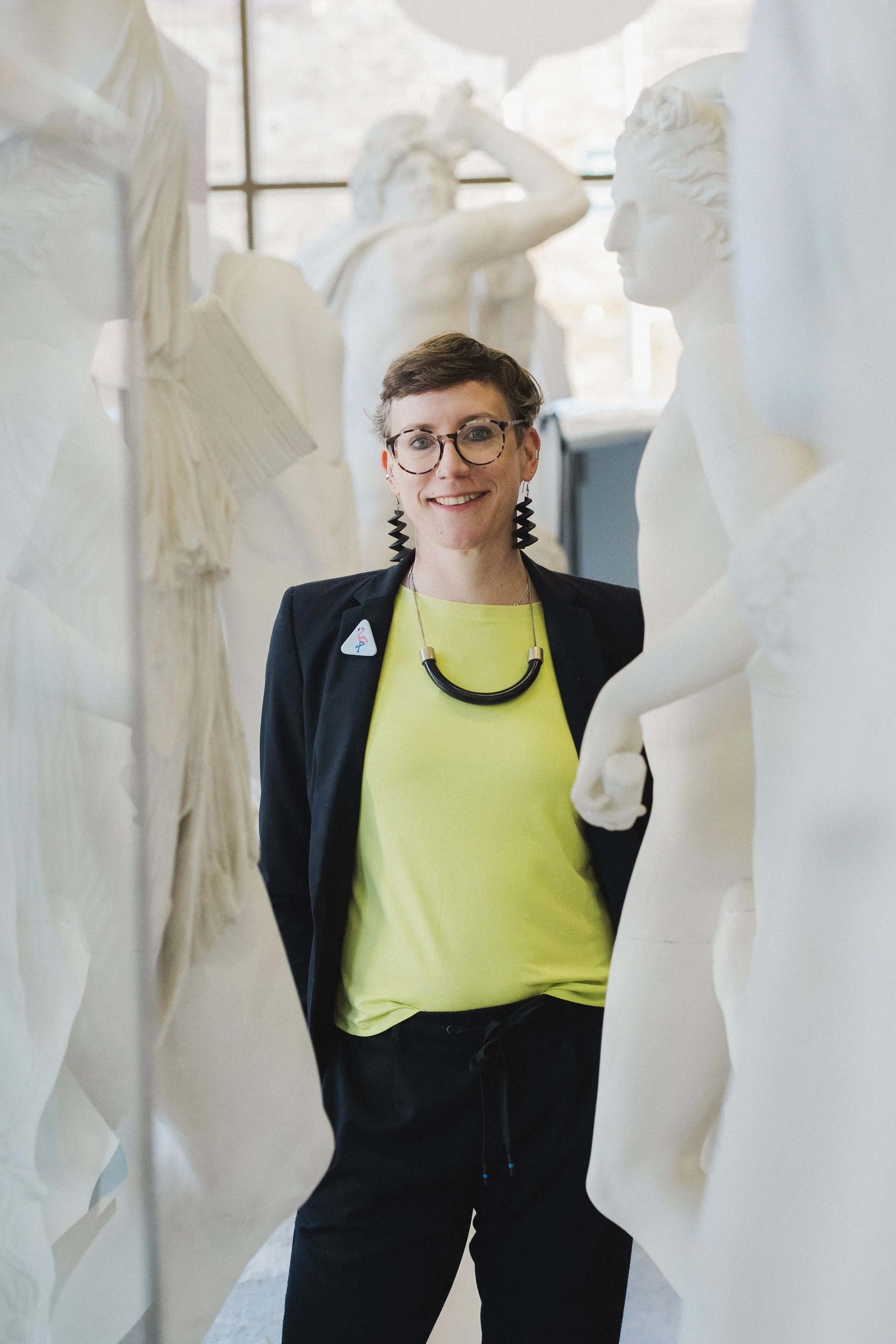 Porträt von Dr. Polly Lohmann, Vorstand der Novus Stiftung, freundlich und lachend zwischen Gipsabgüssen antiker Statuen in der Antikensammlung der Universität Heidelberg.