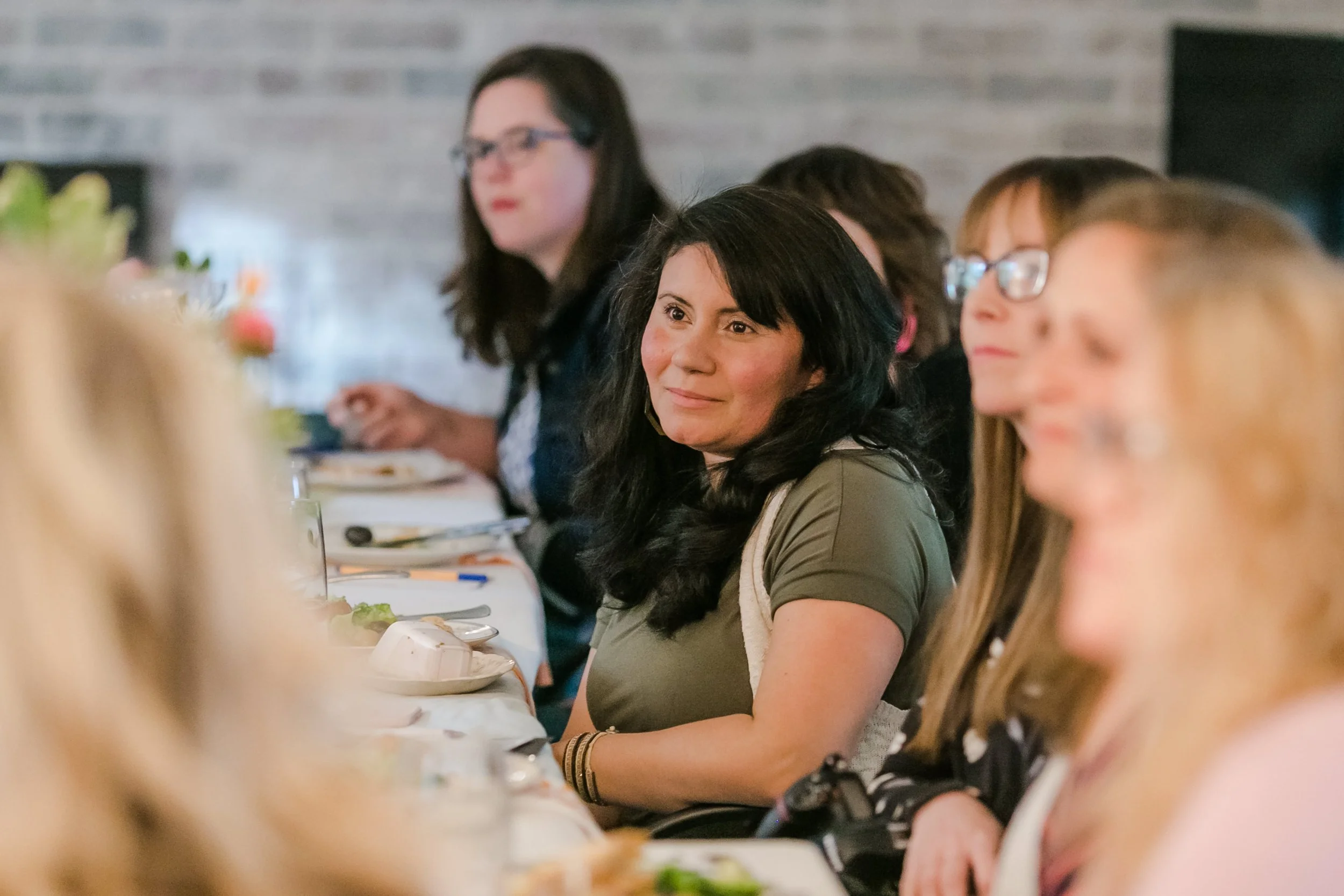 Group of women sitting at a dinner table during a formal event, smiling and listening attentively.