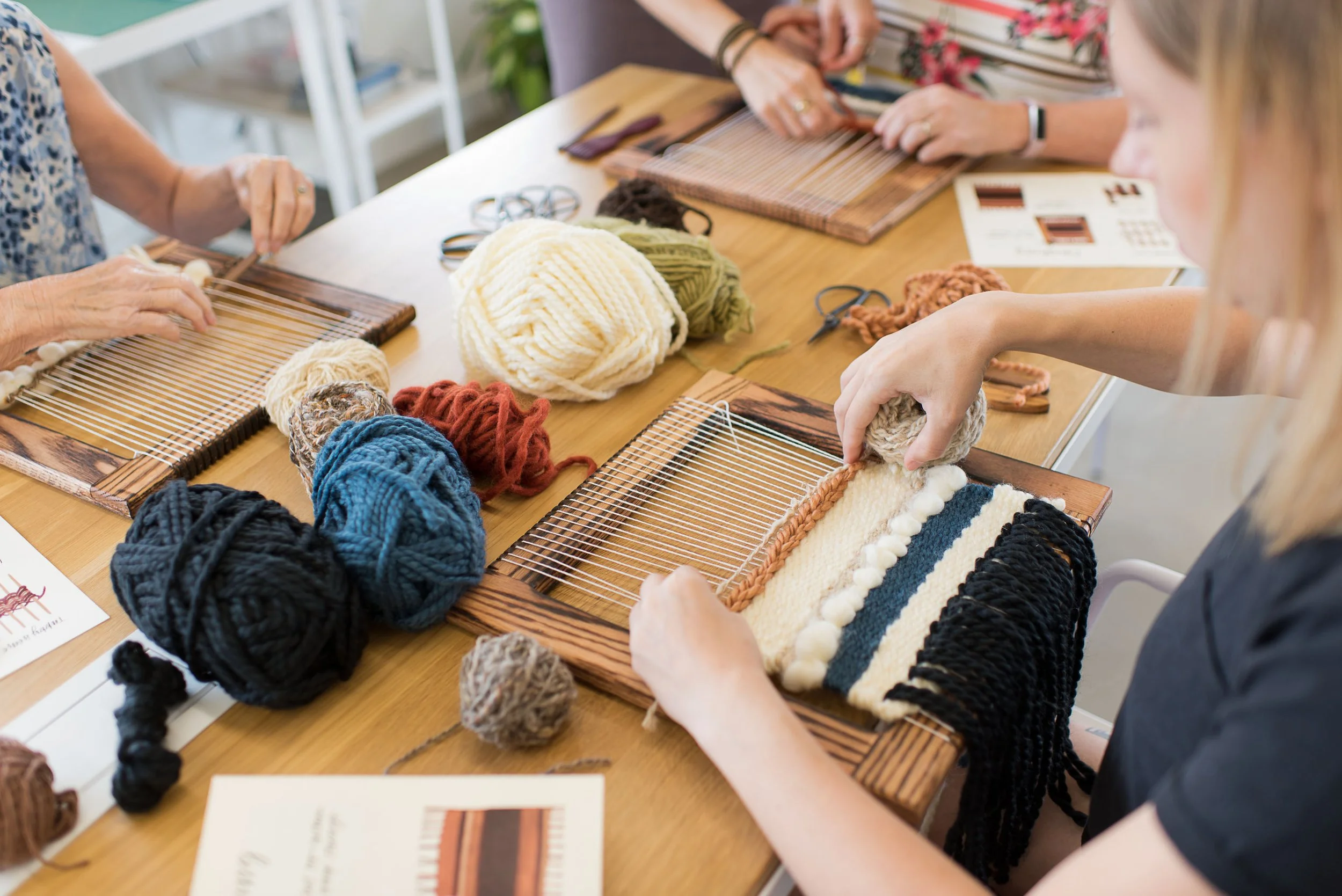 People weaving colorful yarns on small wooden looms at a crafting workshop