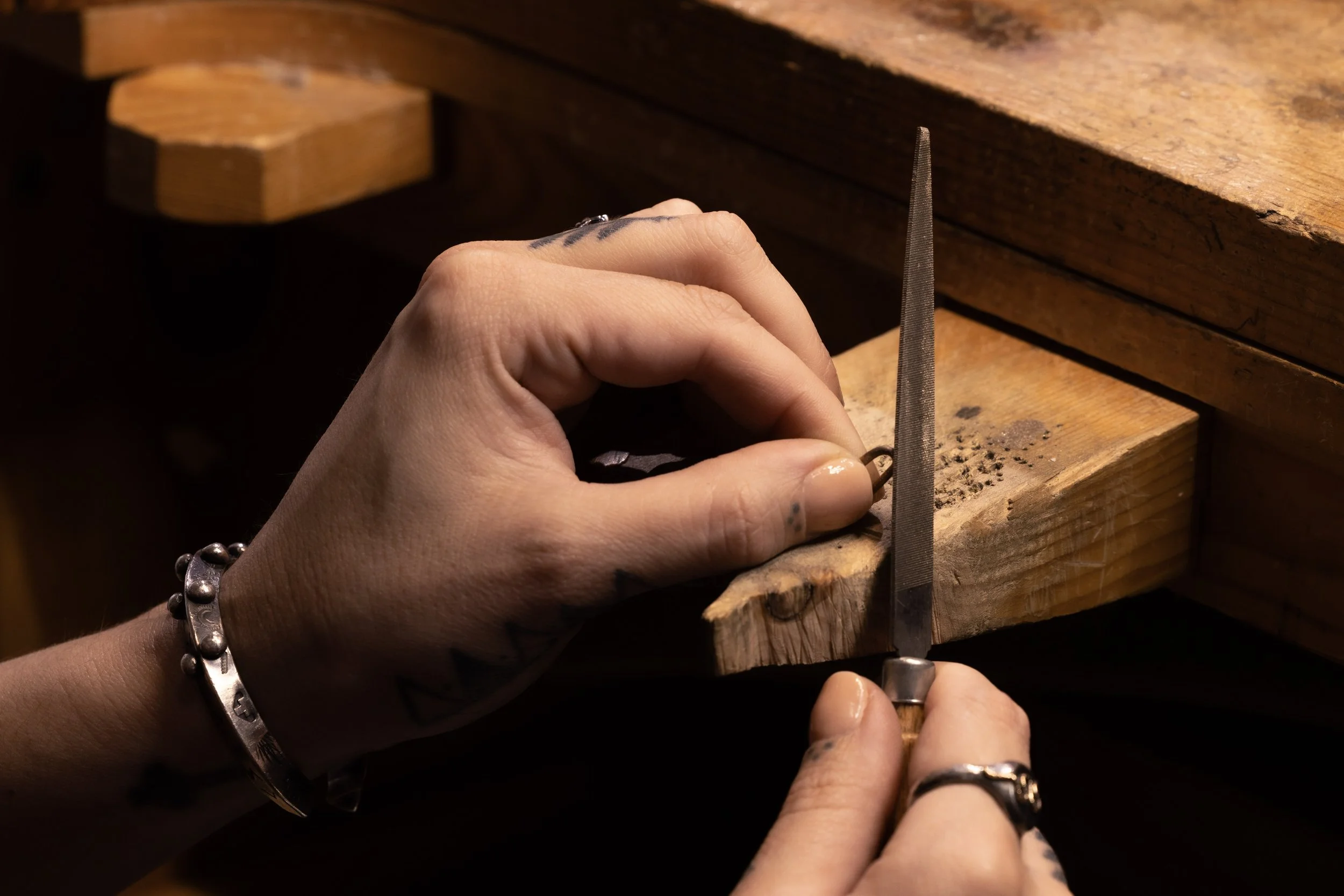 A person's hands working on wood, using a metal rasp and carving a small piece of wood on a workbench.