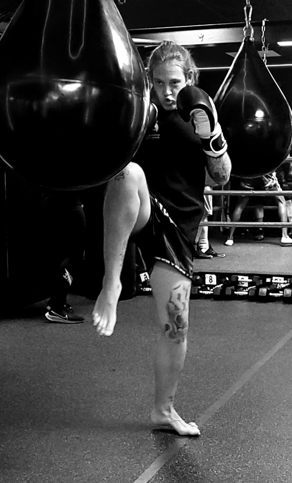 Person practicing martial arts with focus mitts in a gym, mid-kick, black and white photo.