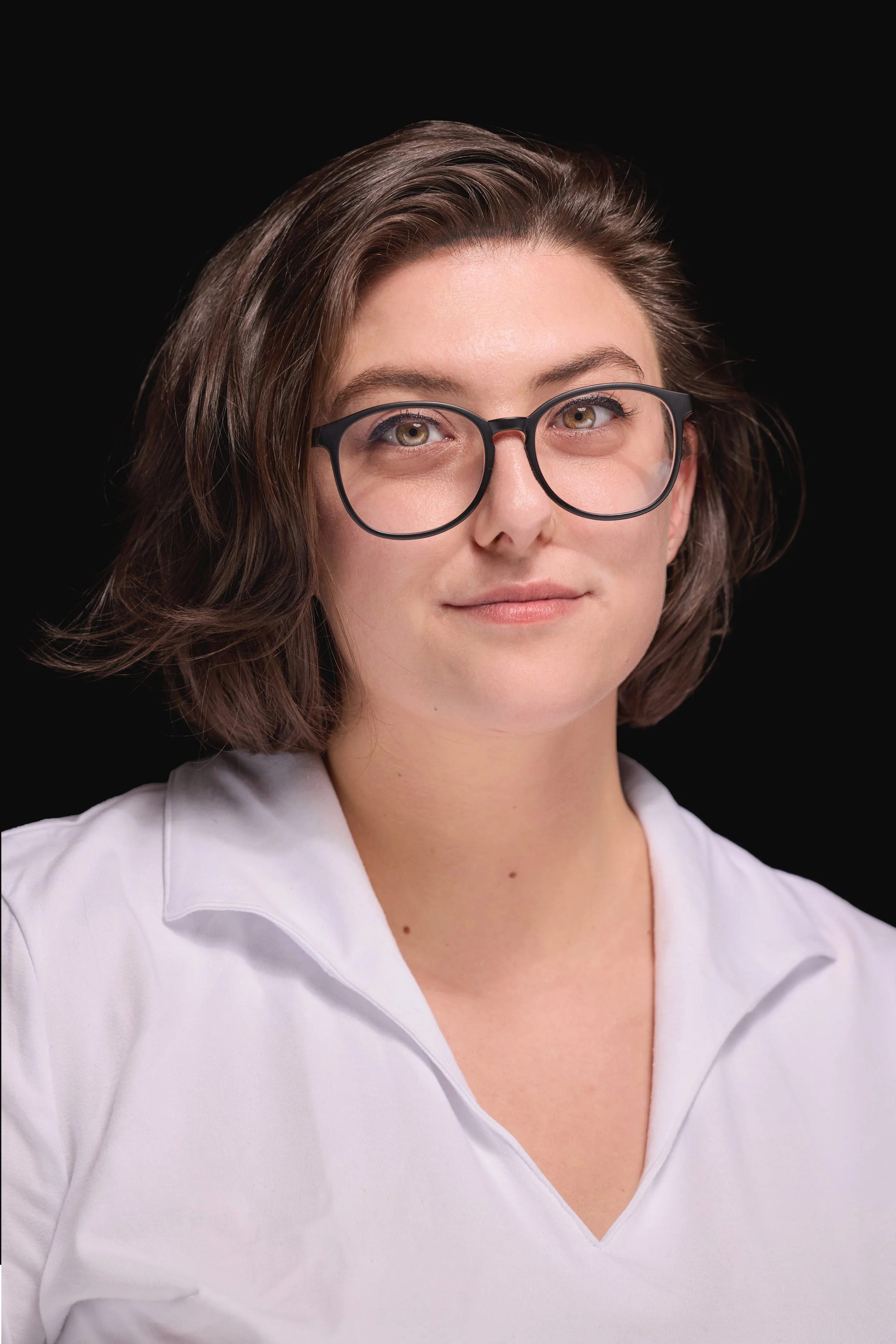 an image of abigail salling. she has short, fluffy brown hair, green eyes which are lined with black liner, and black glasses. she is wearing a white, collared shirt.