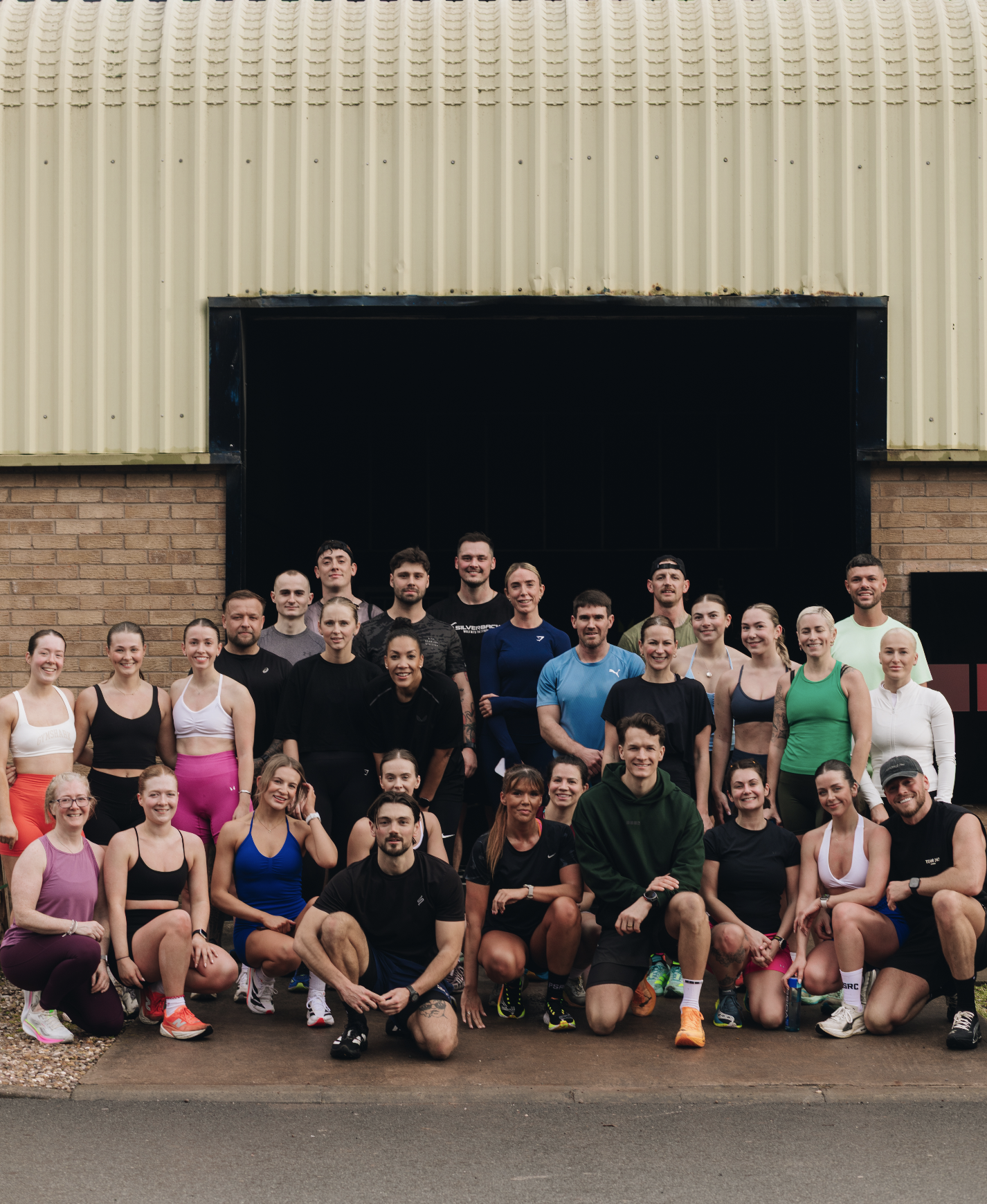 Group of people in athletic wear posing outside a building with brick and metal siding.