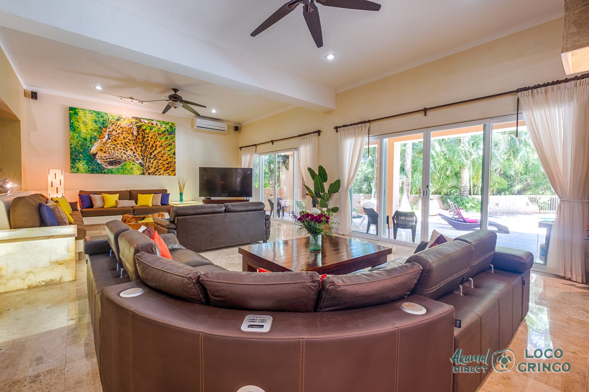 Luxury living room with leather sofas, large wall art featuring leopard, sliding glass doors opening to outdoor patio with chairs.