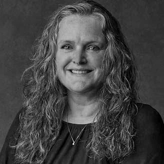 Black and white portrait of a smiling woman with long, curly hair wearing a necklace and dark top.