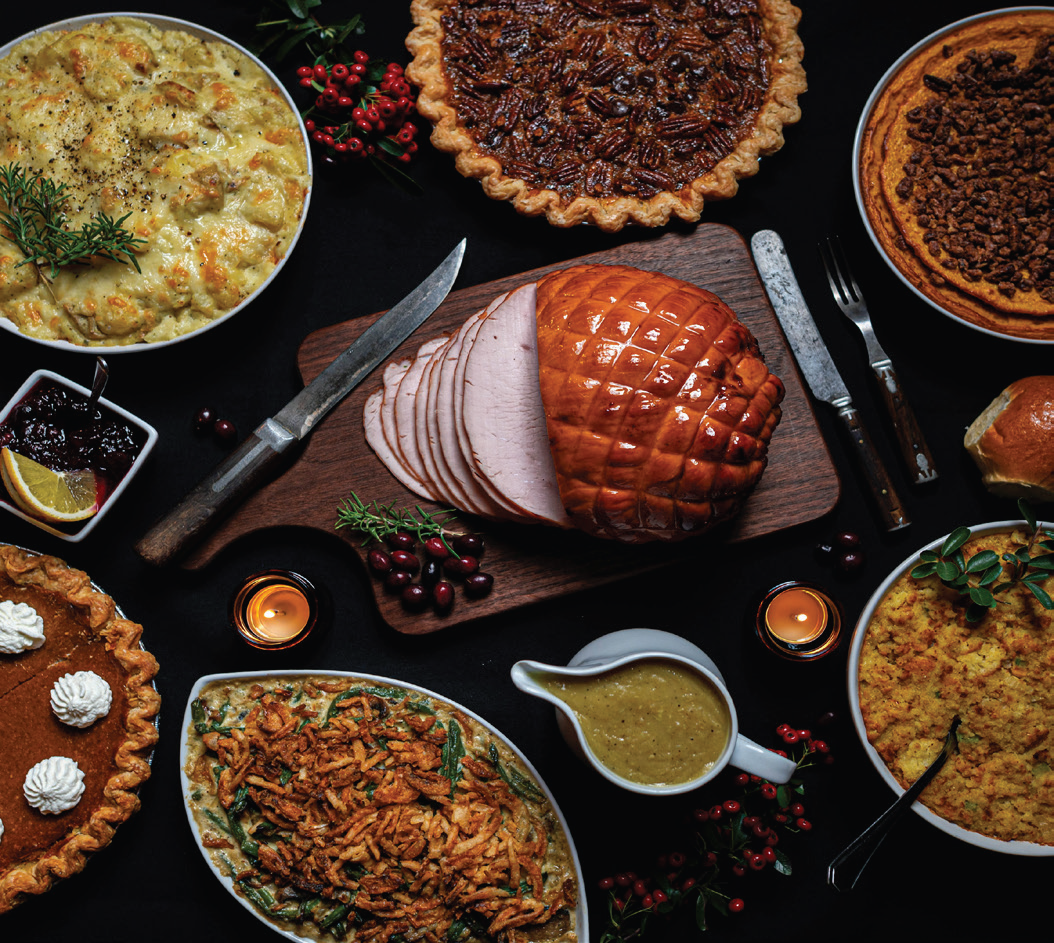 A table loaded with food, including a ham, gravy, side dishes, and pies