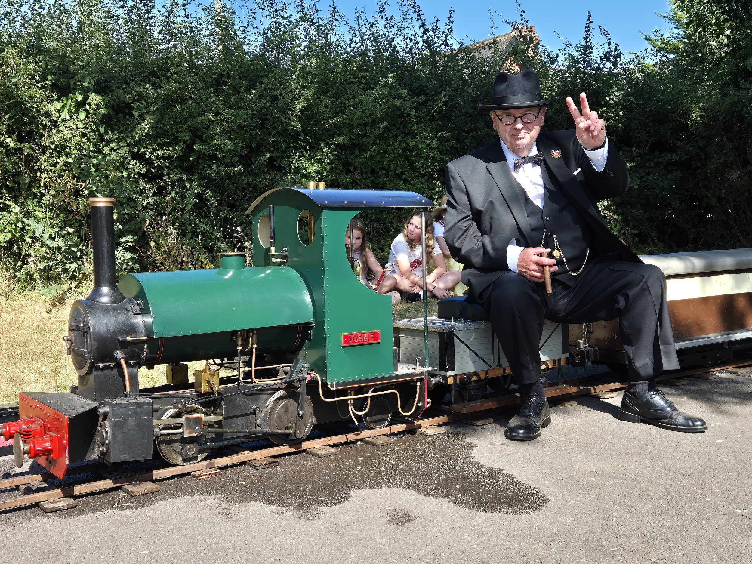 A miniature steam train is seen with a person in costume sitting on the carriage behind the engine at a 1940's event in Cardiff, Wales