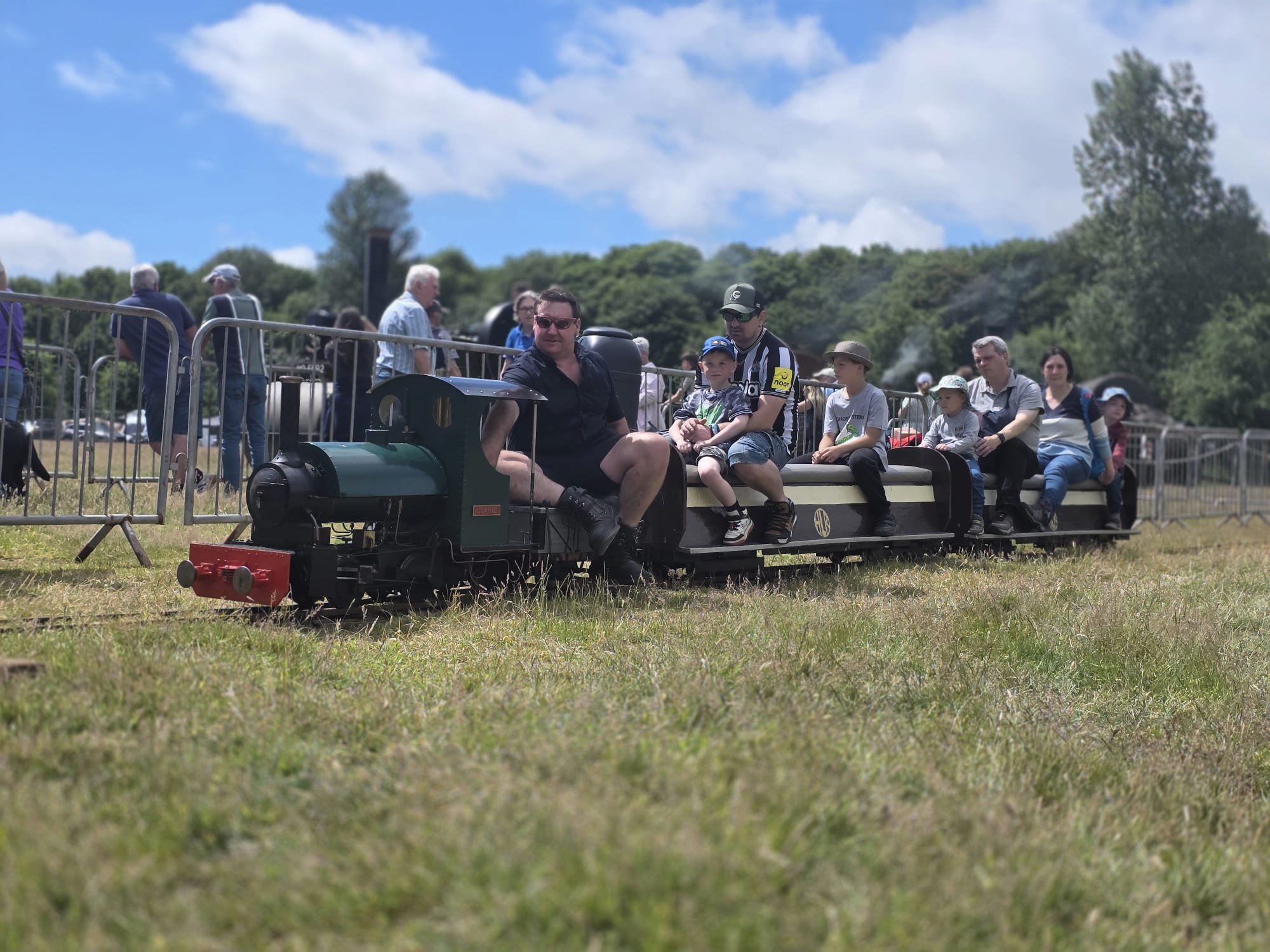 Miniature train at a steam rally in Newcastle upon Tyne with passengers sitting on it, outdoor on grass on a hot summers day..