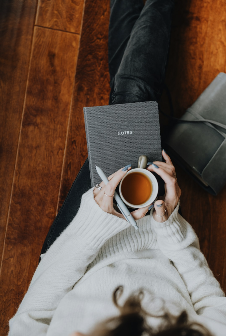 Woman sitting on a floor with a notebook and tea.