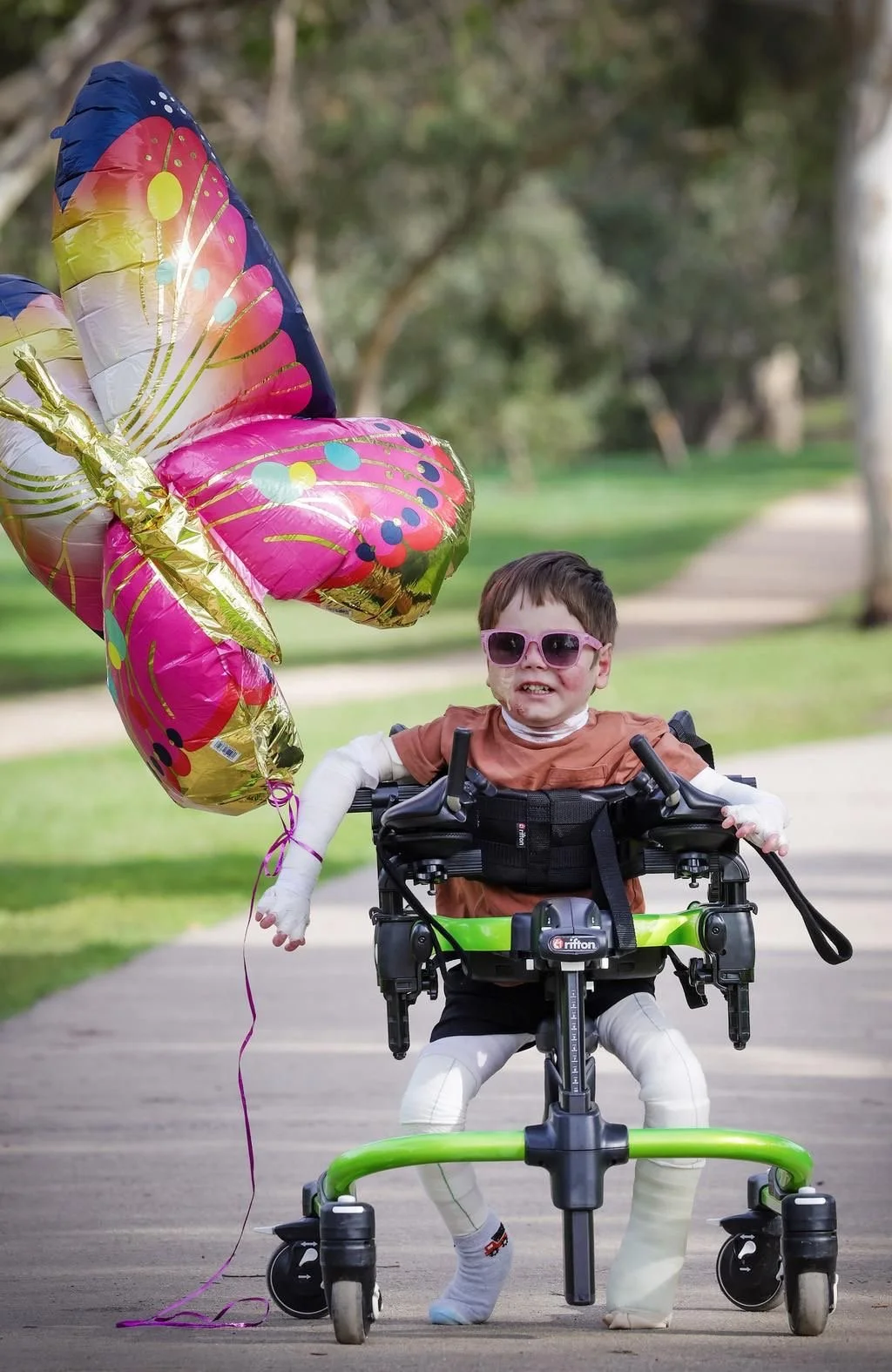 Jacob Burmeister using his walker in a park, with a butterfly balloon.