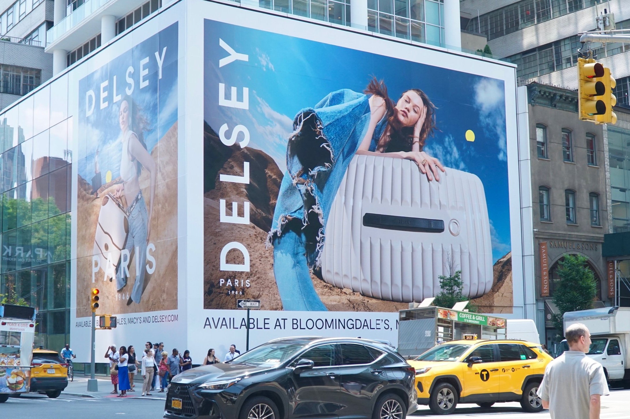 Delsey Paris billboard featuring luggage, on a city street with cars and pedestrians nearby.